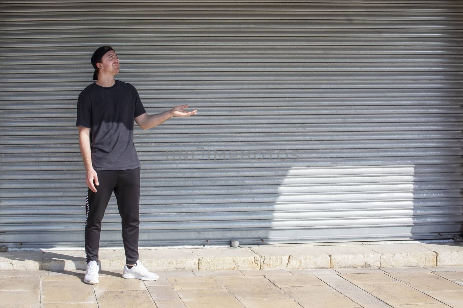 Young casual sporty dressed man with cap backwards in black against corrugated iron wall street style