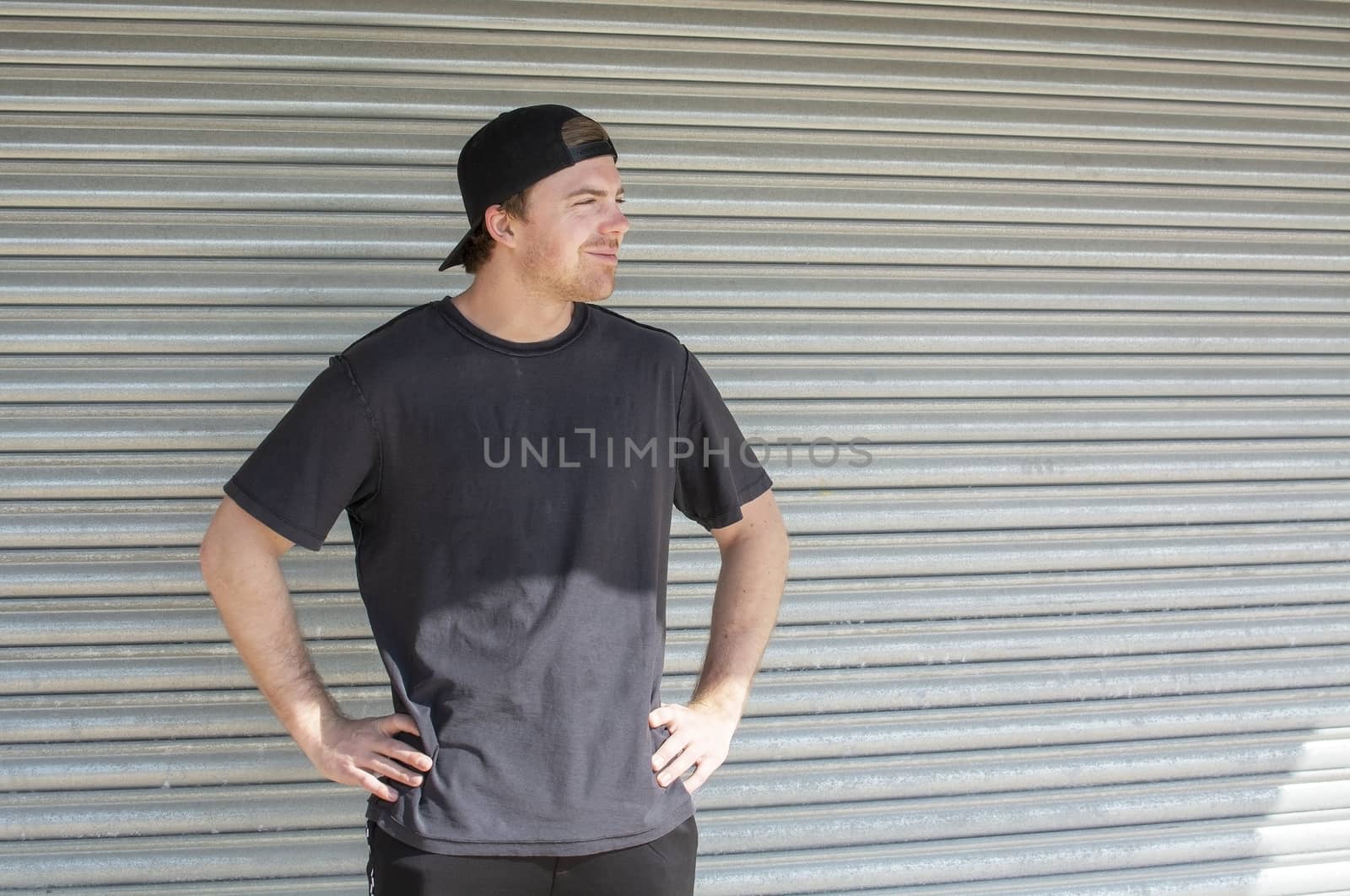 Young casual sporty dressed man with cap backwards in black against corrugated iron wall street style