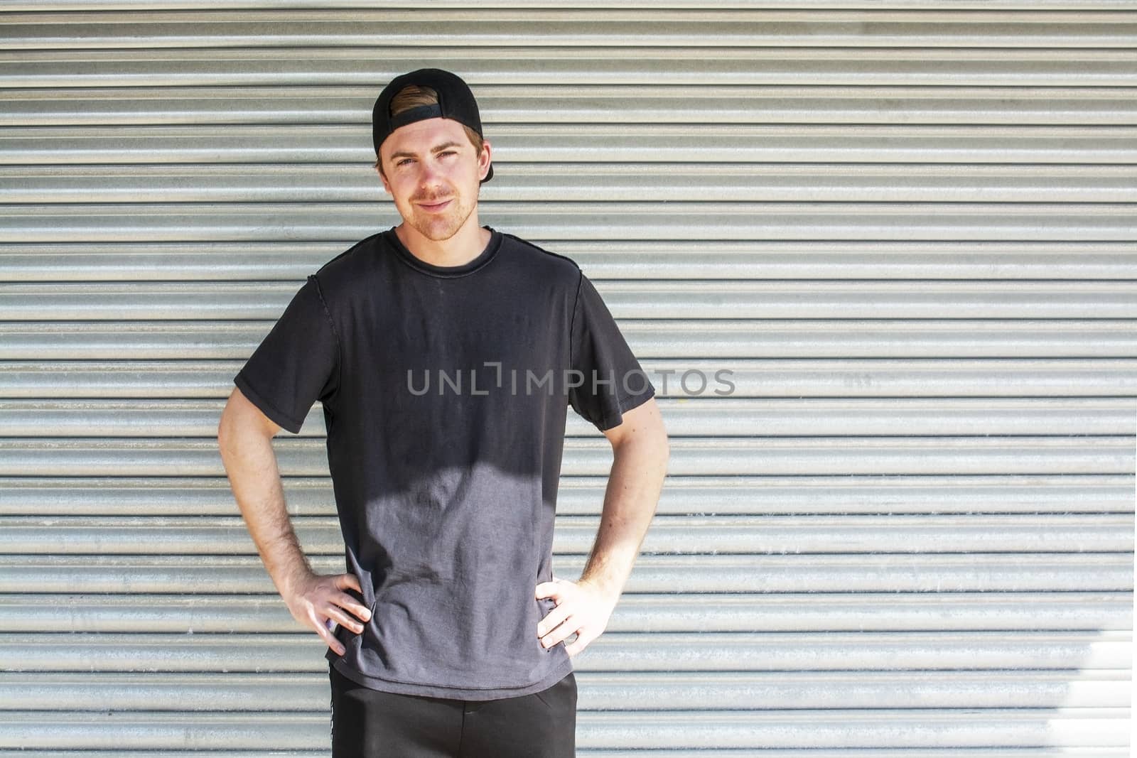 Young casual sporty dressed man with cap backwards in black against corrugated iron wall street style