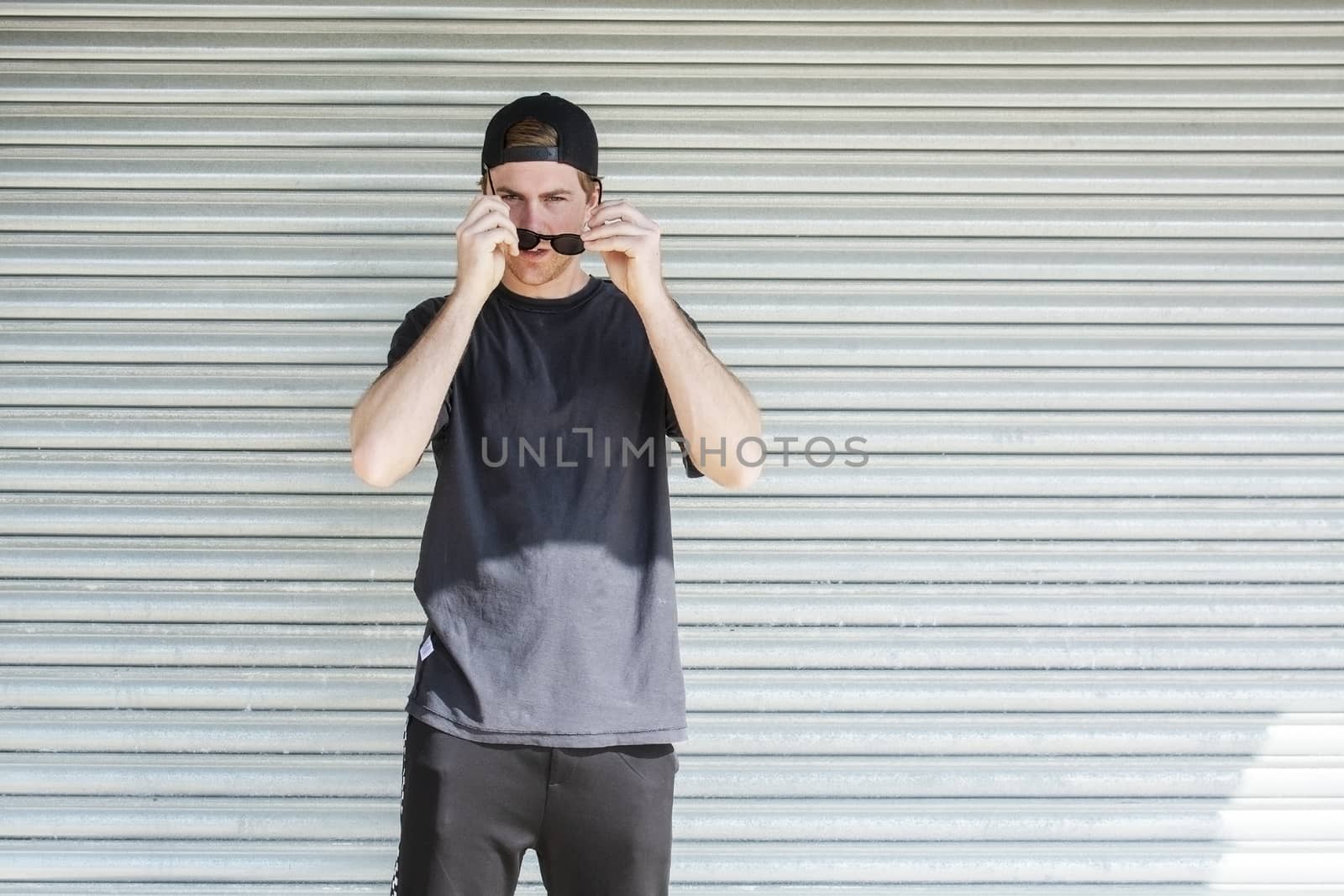 Young casual sporty dressed man with cap backwards in black against corrugated iron wall street style