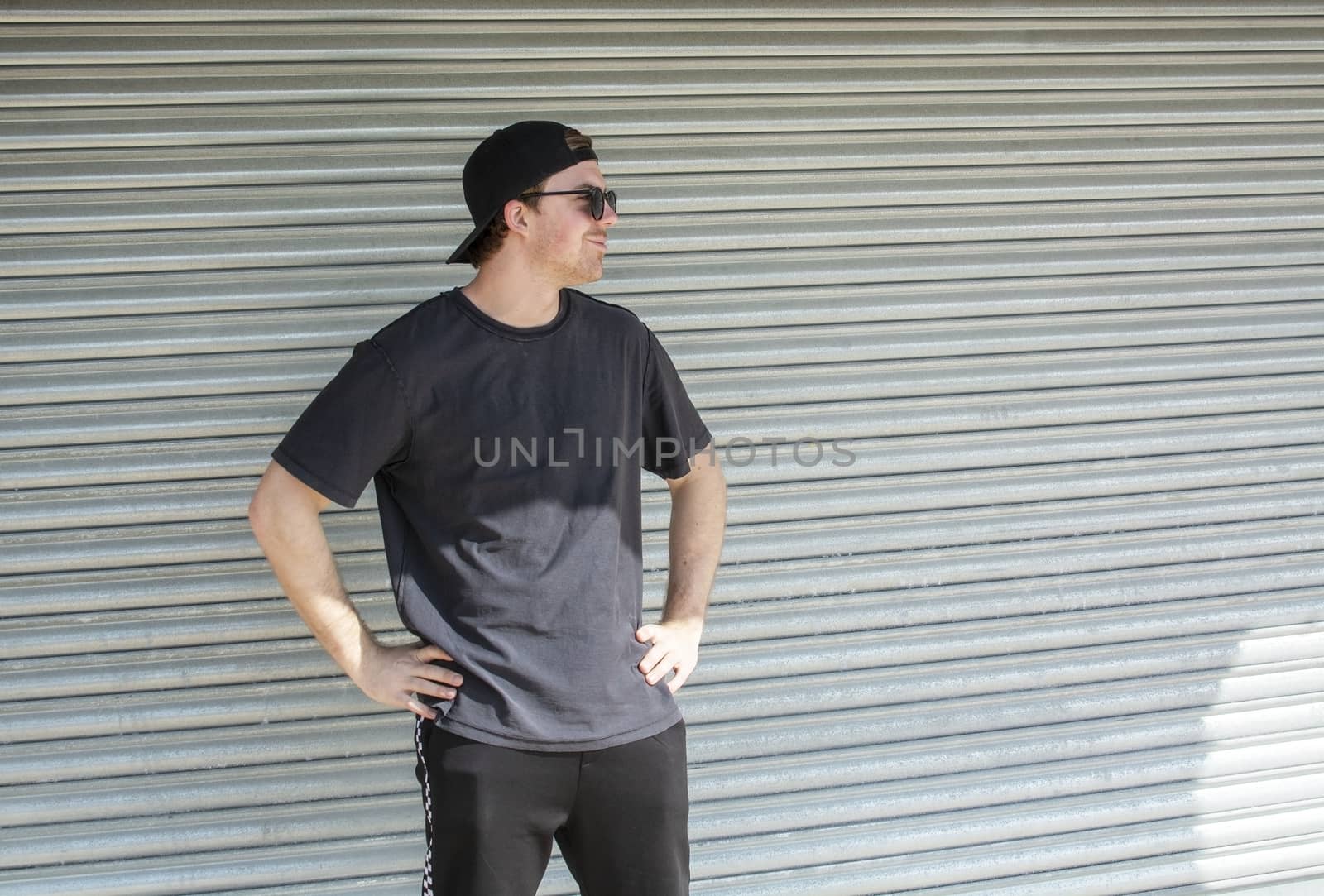 Young casual sporty dressed man with cap backwards in black against corrugated iron wall street style