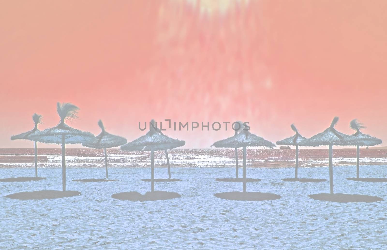 Sunrays pouring on sandy beach with straw parasols summer travel background toned in color Living Coral.