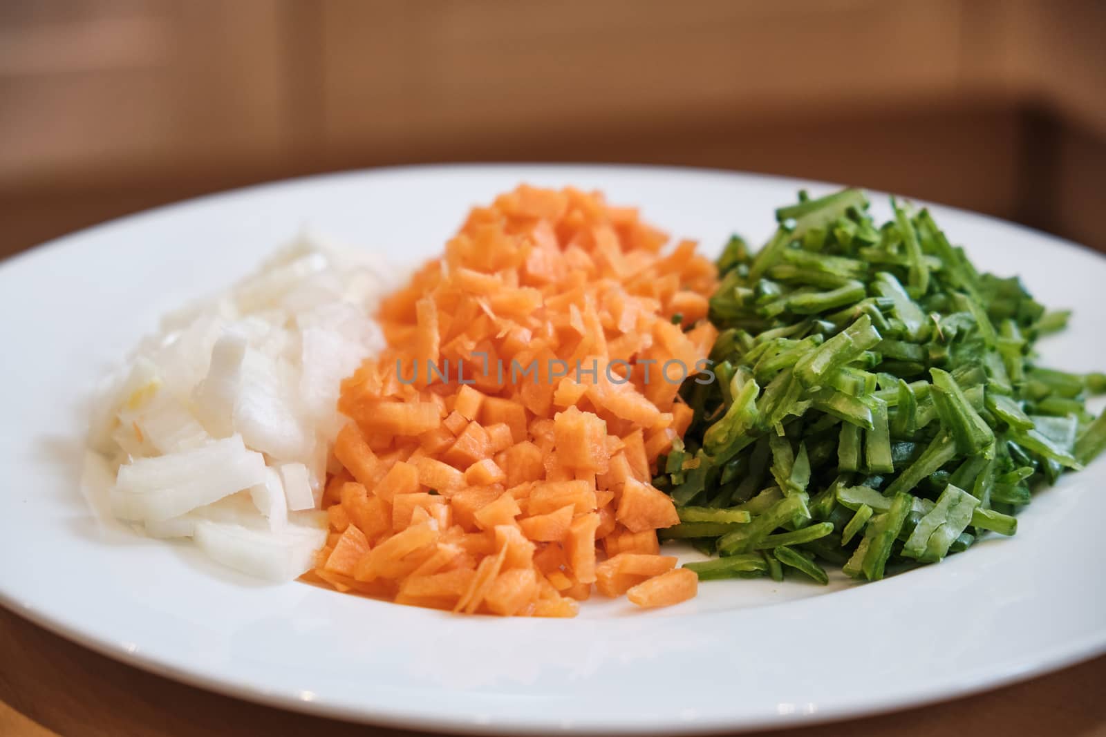 A plate of chopped onions, carrots and beans on a table.