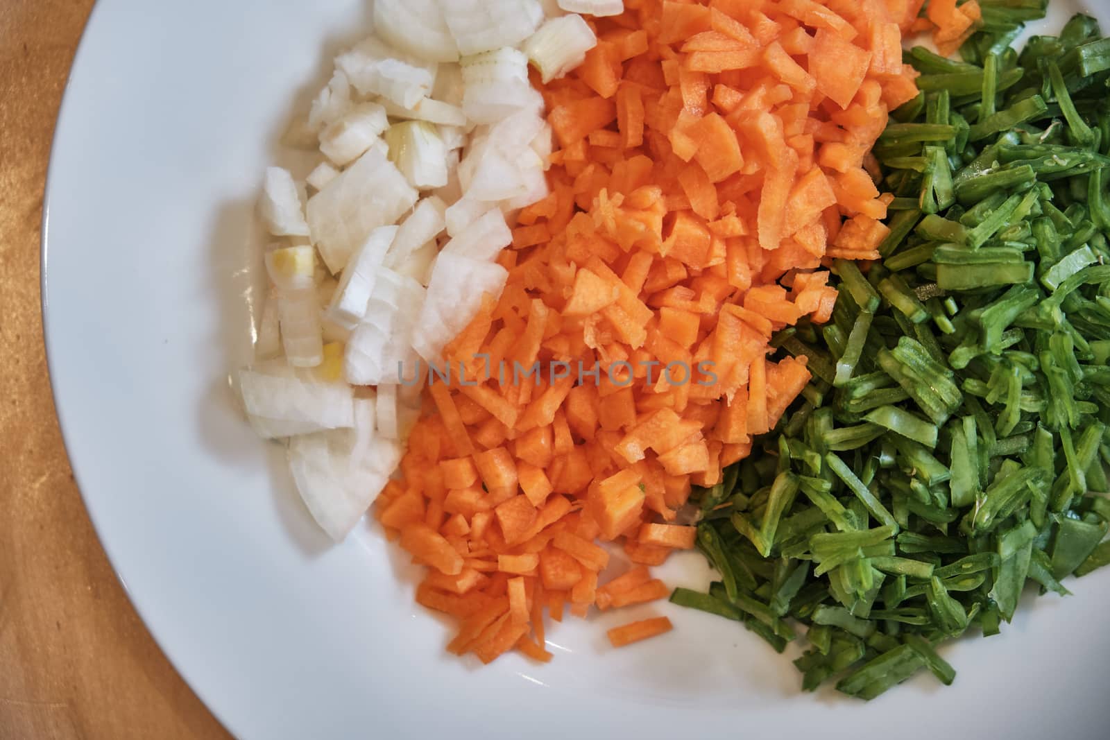 A plate of chopped onions, carrots and beans on a table.