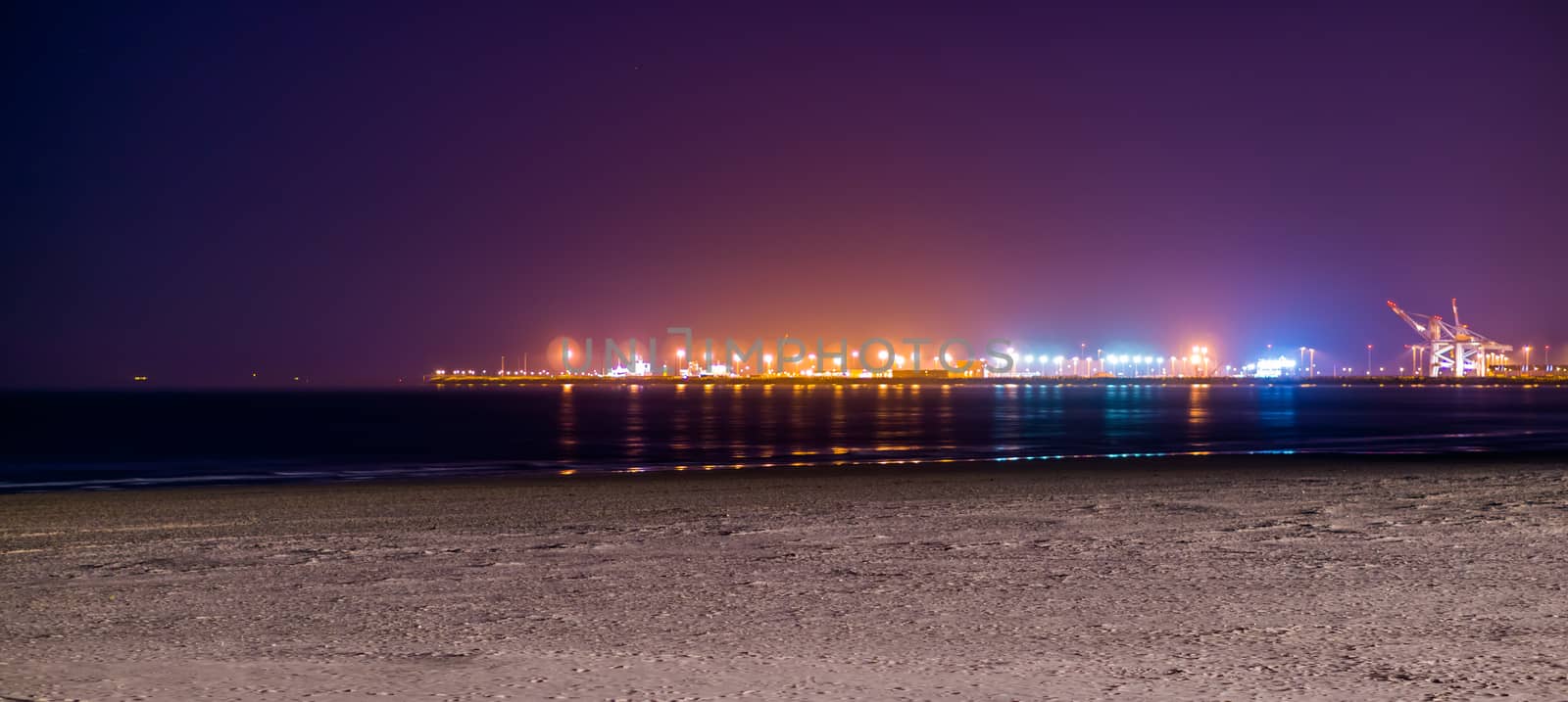 the coastline of Blankenberge beach lighted by night, colorful lights on the industry terrain in the distance by charlottebleijenberg