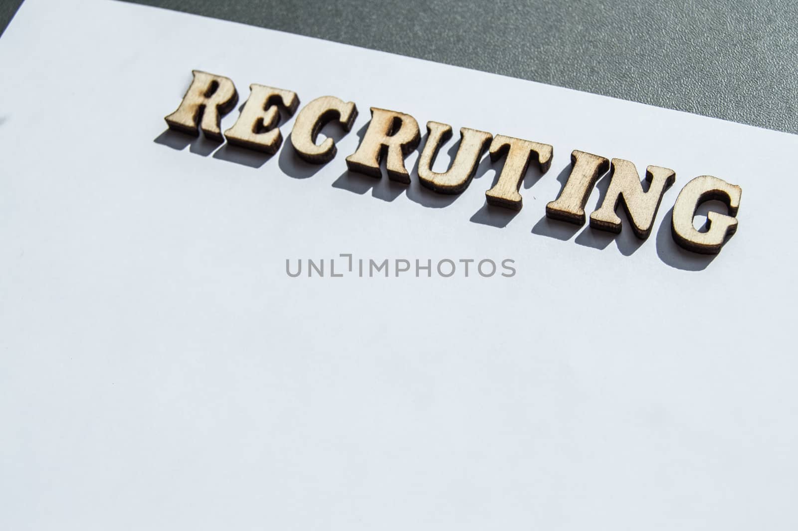 The word recruiting is written in wooden letters on a white background, the concept of hiring employees, recruitment in business and army by claire_lucia