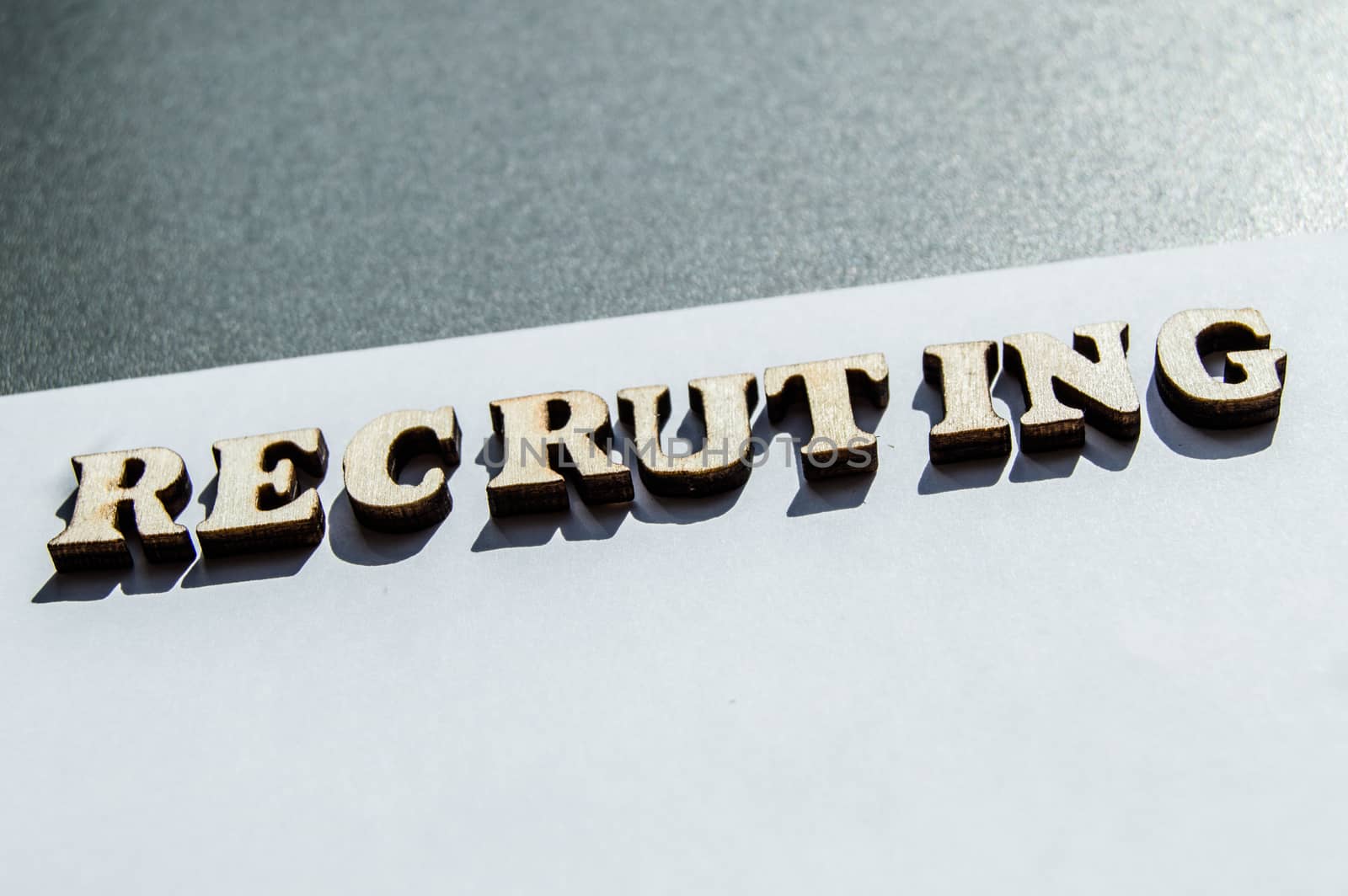The word recruiting is written in wooden letters on a white background, the concept of hiring employees, recruitment in business and army by claire_lucia
