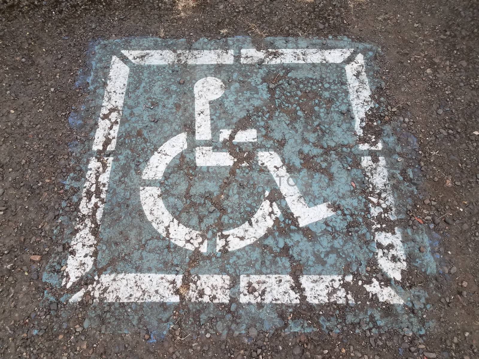 worn blue wheelchair or handicap sign on cracked asphalt
