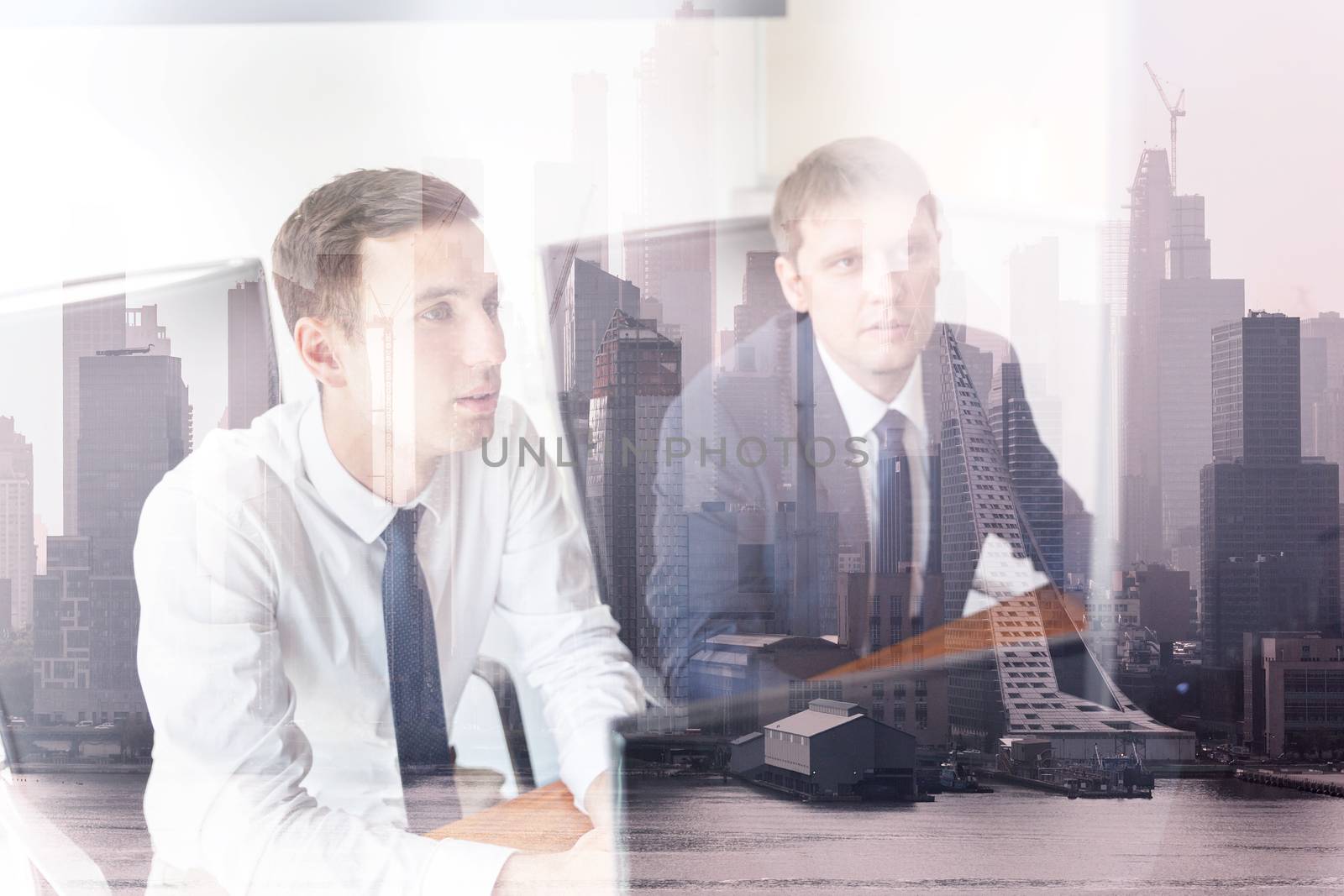 Image of two thoughtful businessmen looking at data on computer screens at business meeting in moder office against new york city manhattan buildings and skyscrapers window reflection.