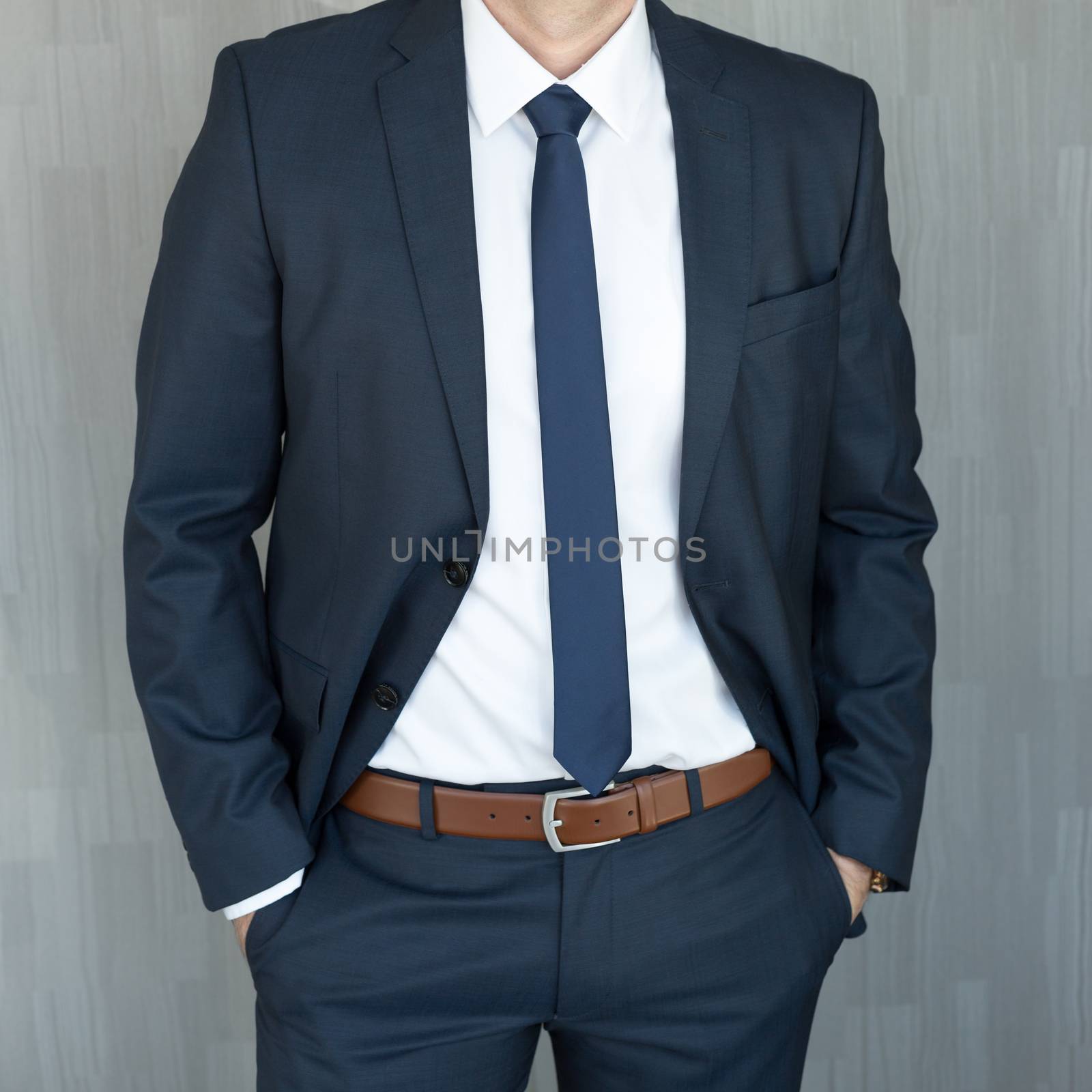 Torso of anonymous white collar worker standing with hands in pockets, wearing beautiful fashionable classic navy blue suit against grey backgound.
