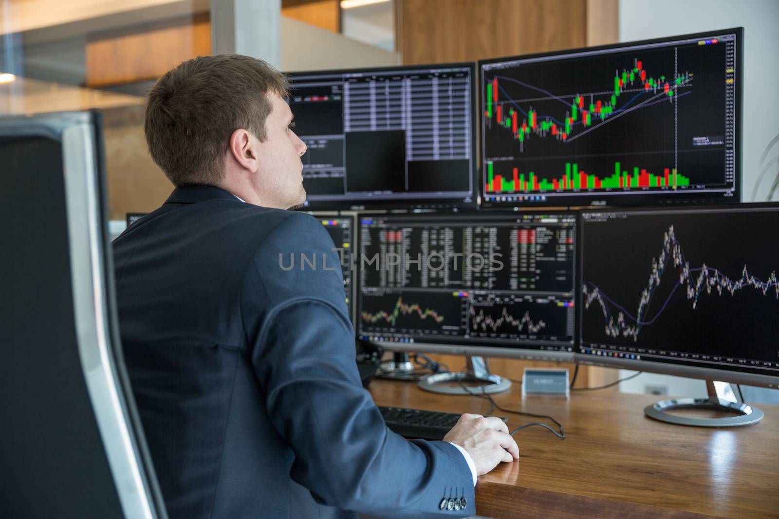 Stock trader looking at computer screens in trdading office. by kasto