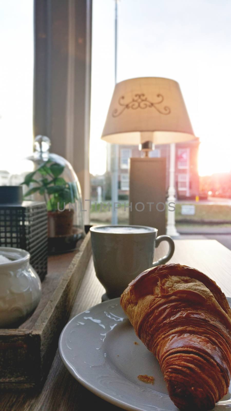 Cup of coffee and fresh baked croissants on plate for breakfast on the table near the window with city view