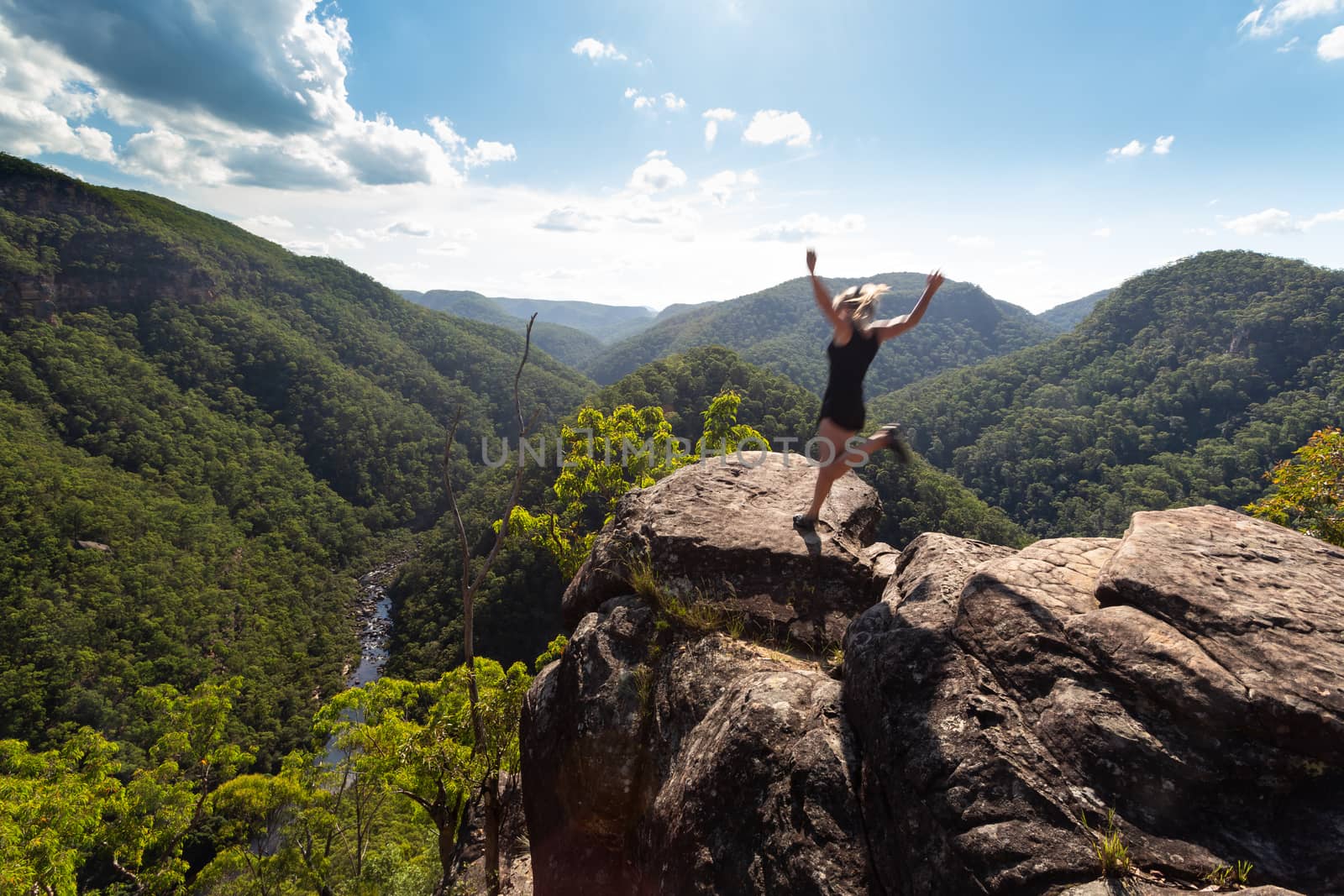 Spirited woman jumping on a high cliff ledge. by lovleah