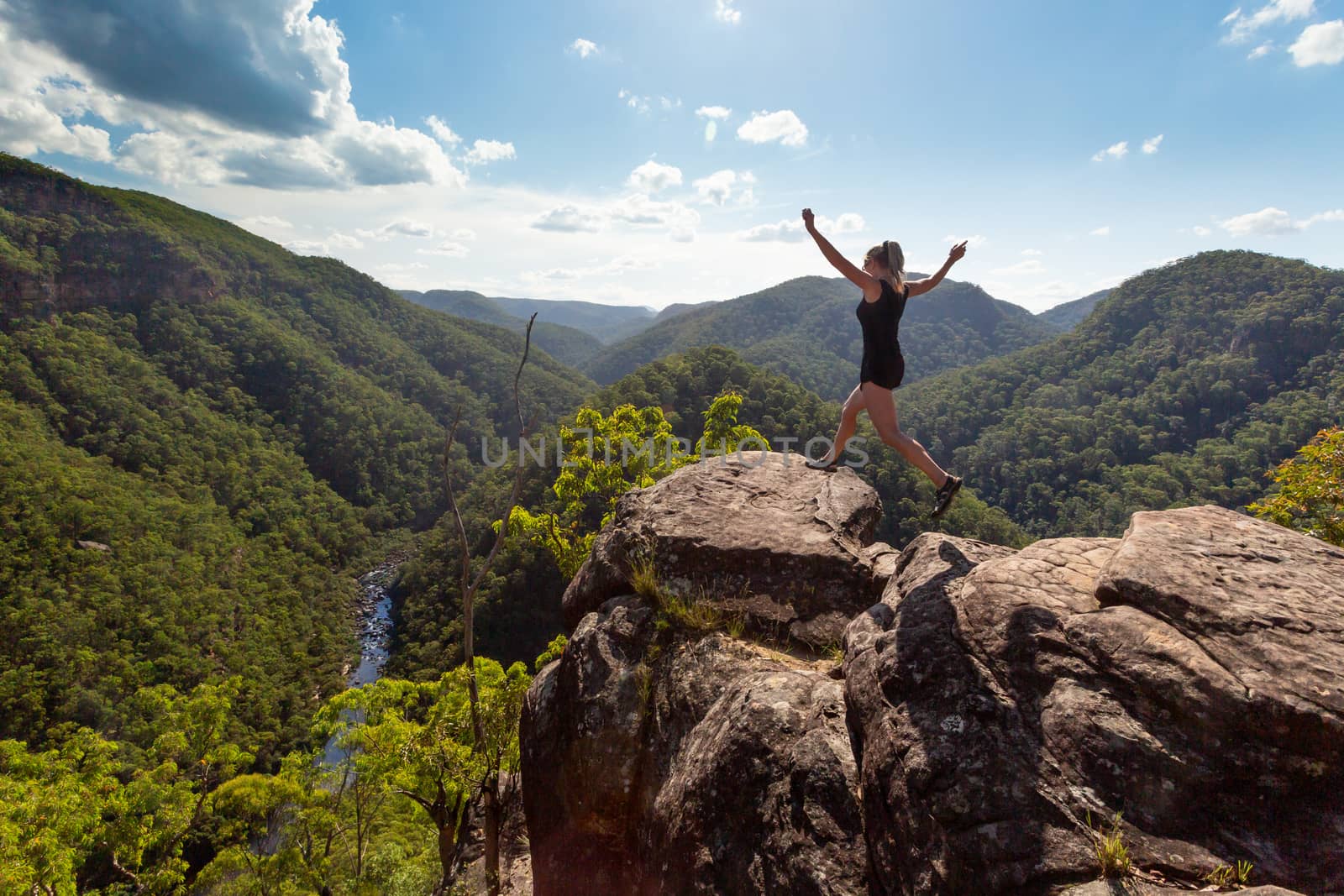 Girl leaping on high rocky cliff with mountain river backdrop by lovleah