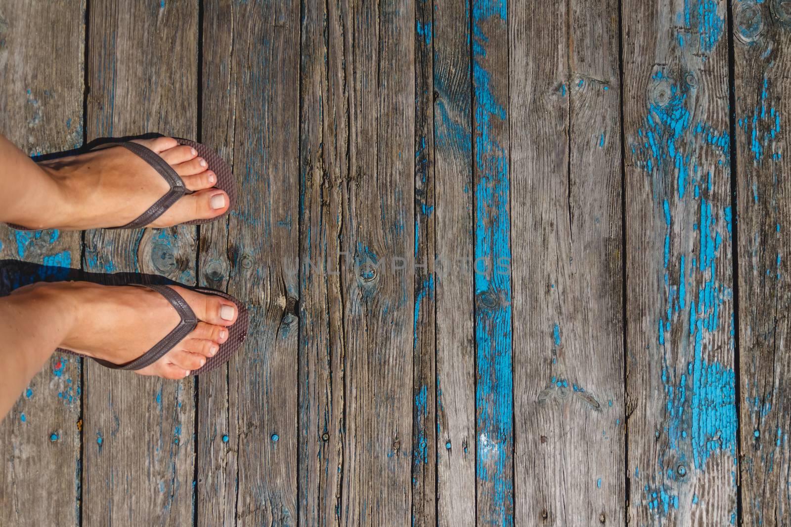 Top view, photo of female legs in beach flip flops on a wooden old floor. Photos on vacation, beach, summer.