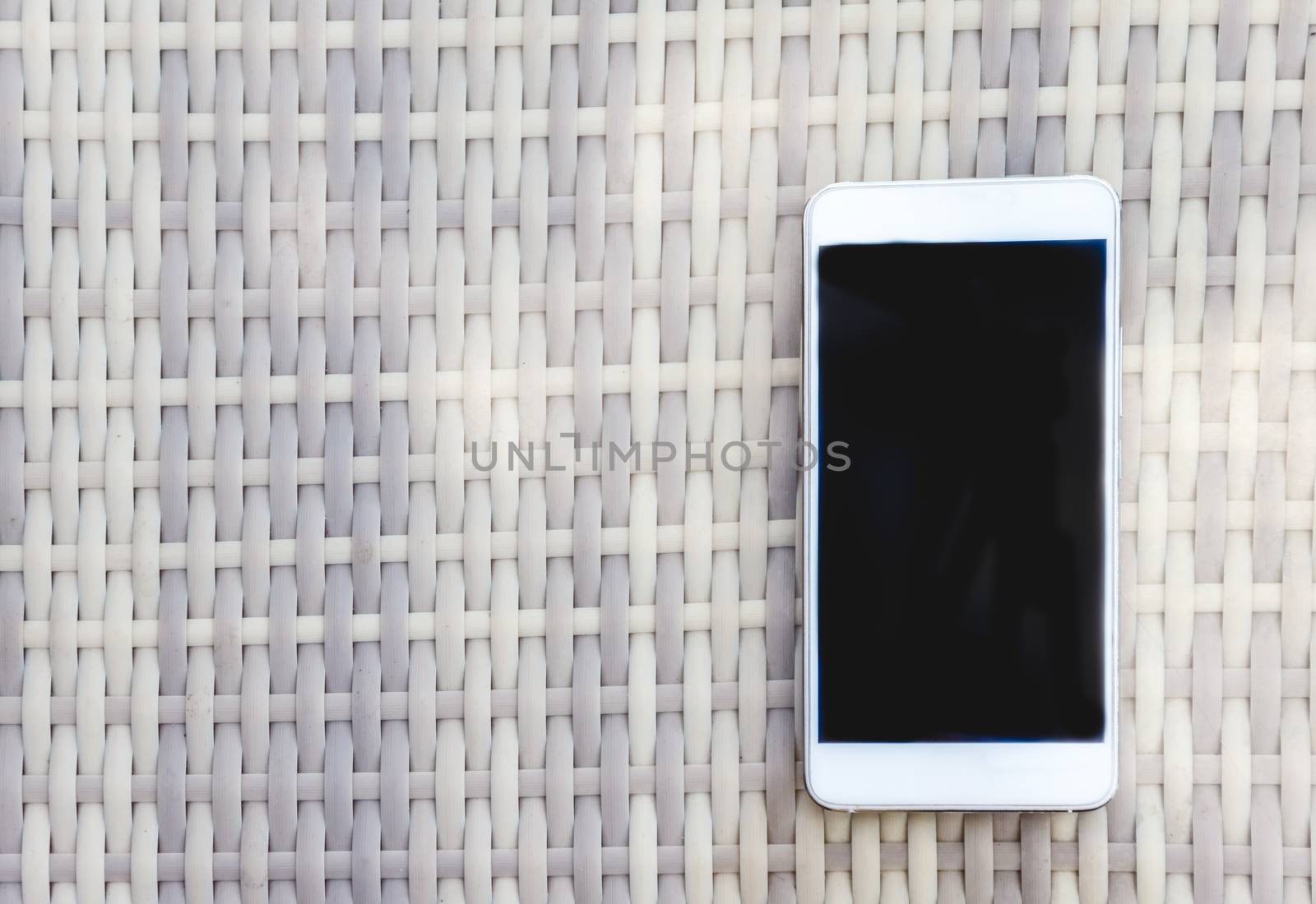 White smartphone lies on a wicker outdoor table. View from above by Tanacha