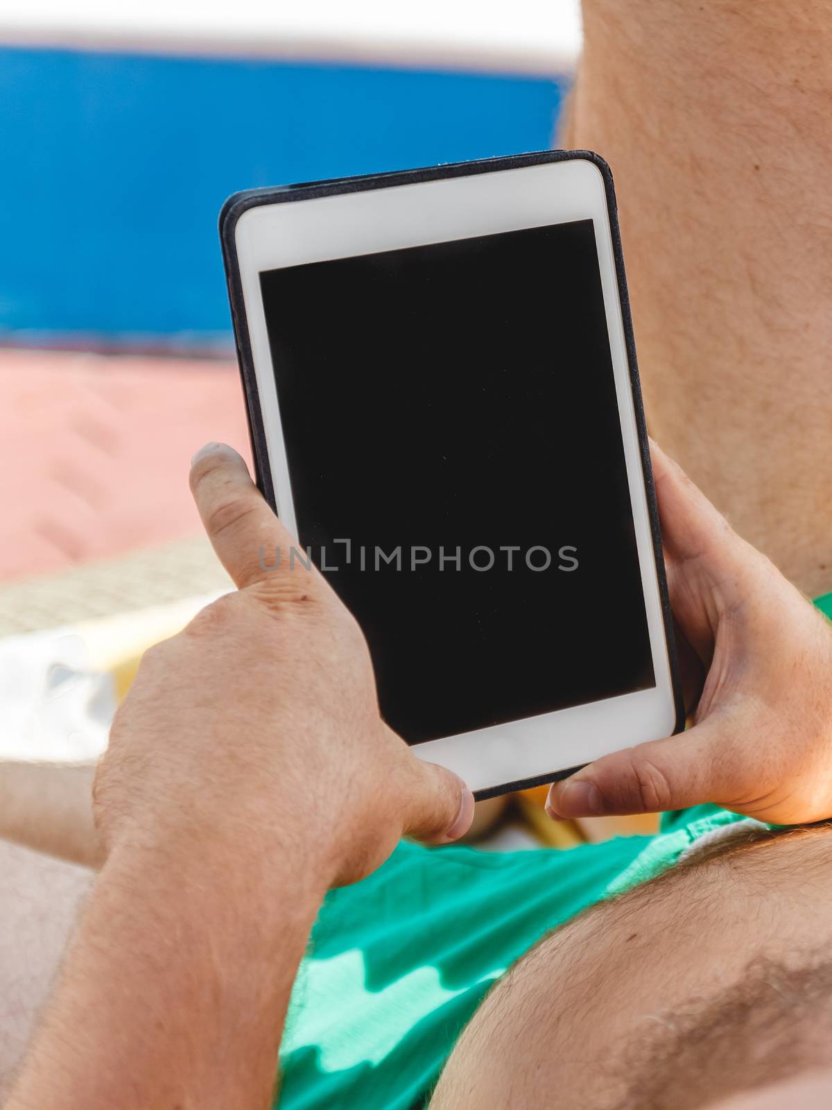 A young man in sunglasses holds a tablet in his hands. Freelancer job concept on the beach and vacation.