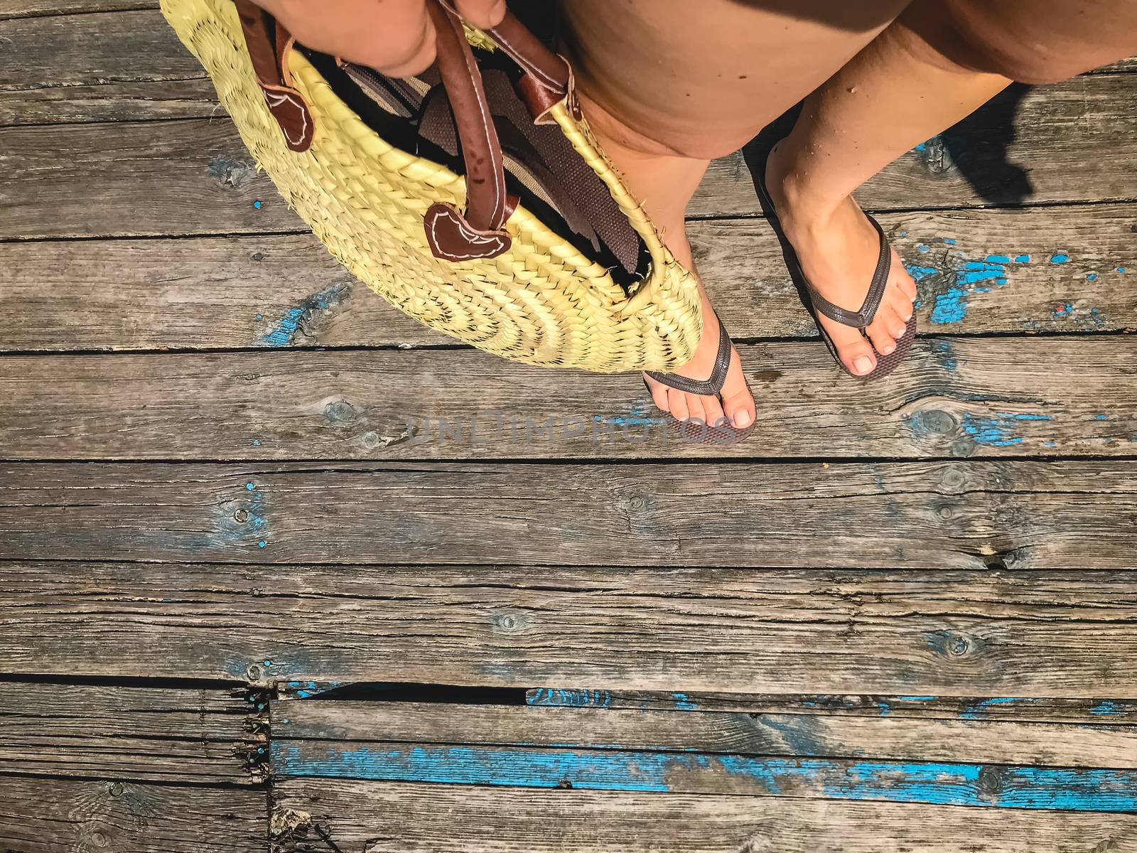 Top view, photo of legs in beach flip-flops and with a straw bag by Tanacha