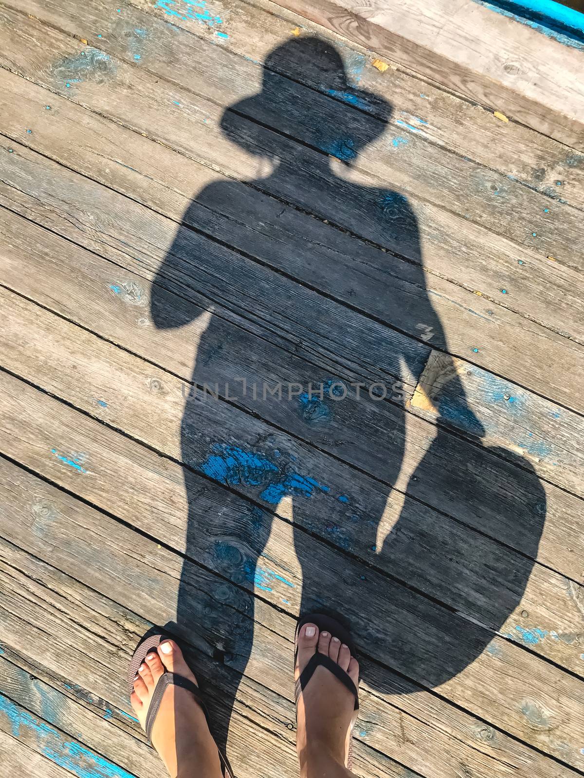 Top view, photo of bare feet and a pair of shadows on a wooden old floor. Photos on vacation, beach, summer.