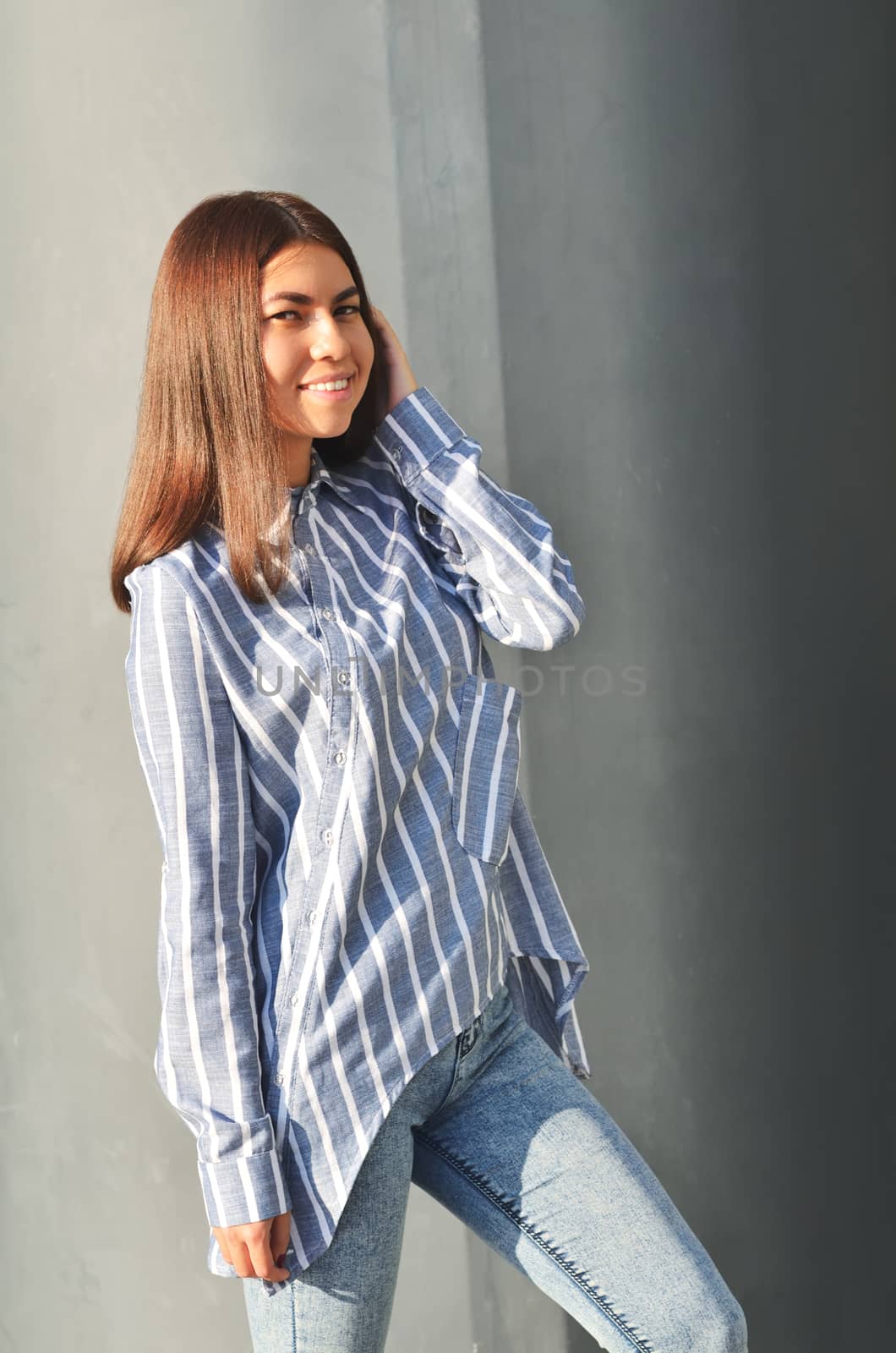 Young beautiful asian girl stands near the wall and posing and she dressed a striped shirt