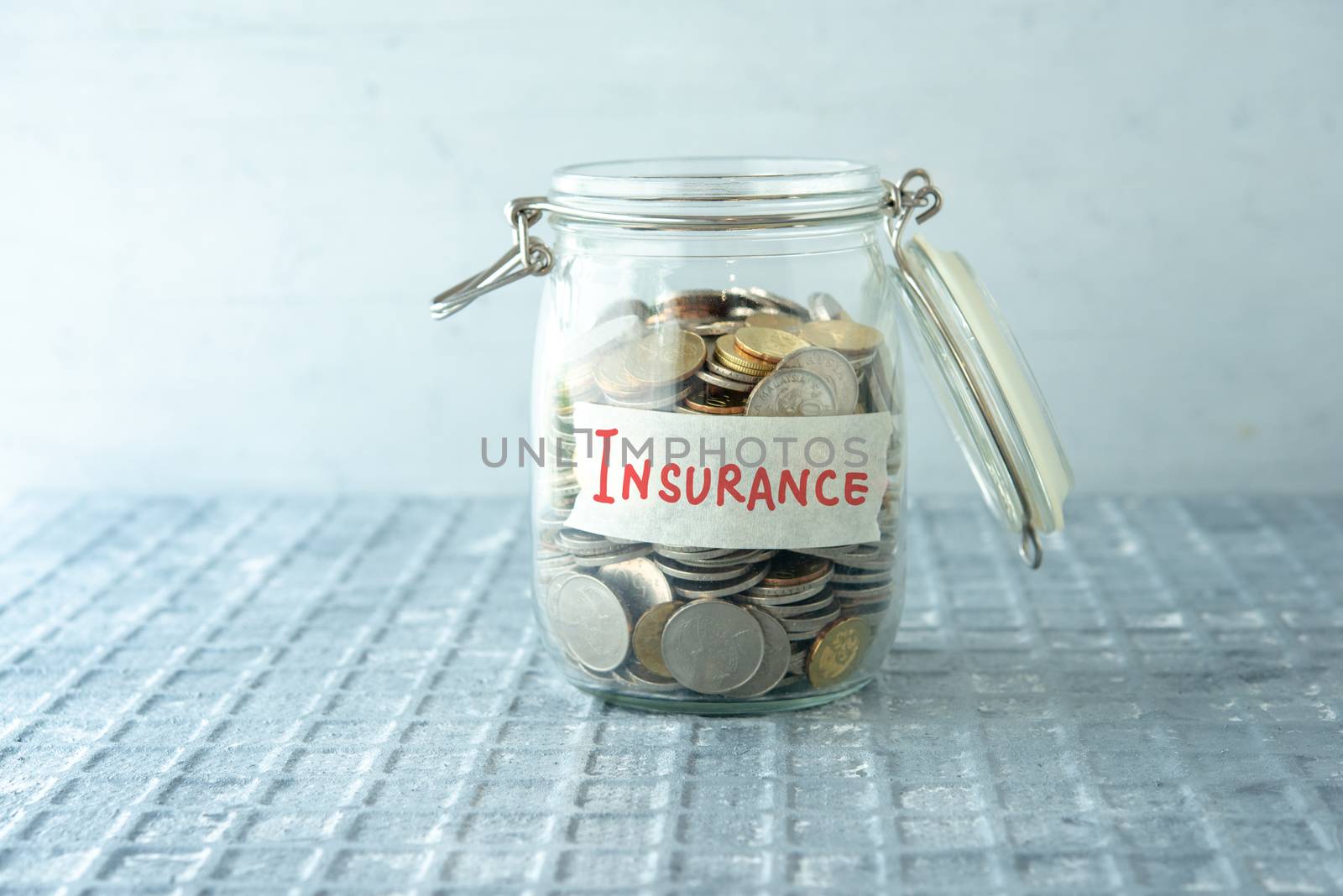 Coins in glass money jar with insurance label, financial concept.