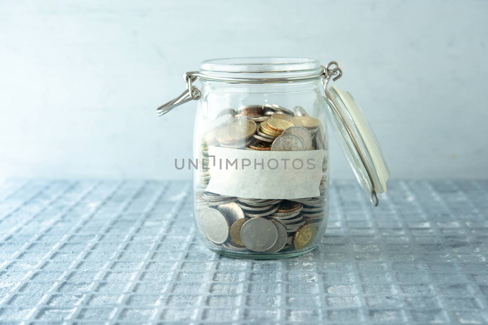 Coins in glass money jar with blank label, financial concept.