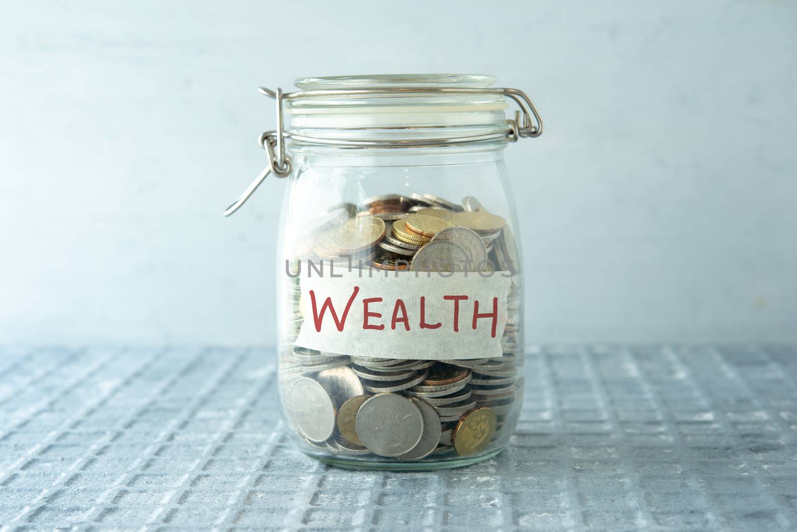 Coins in glass money jar with wealth label, financial concept.