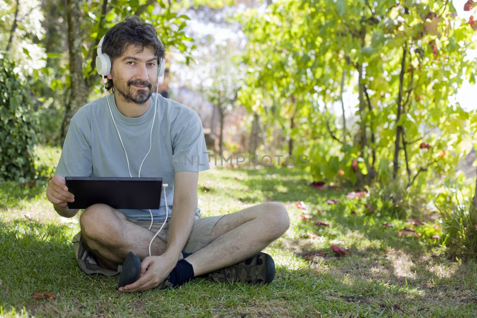 young man holding a tablet with headphones, outdoor