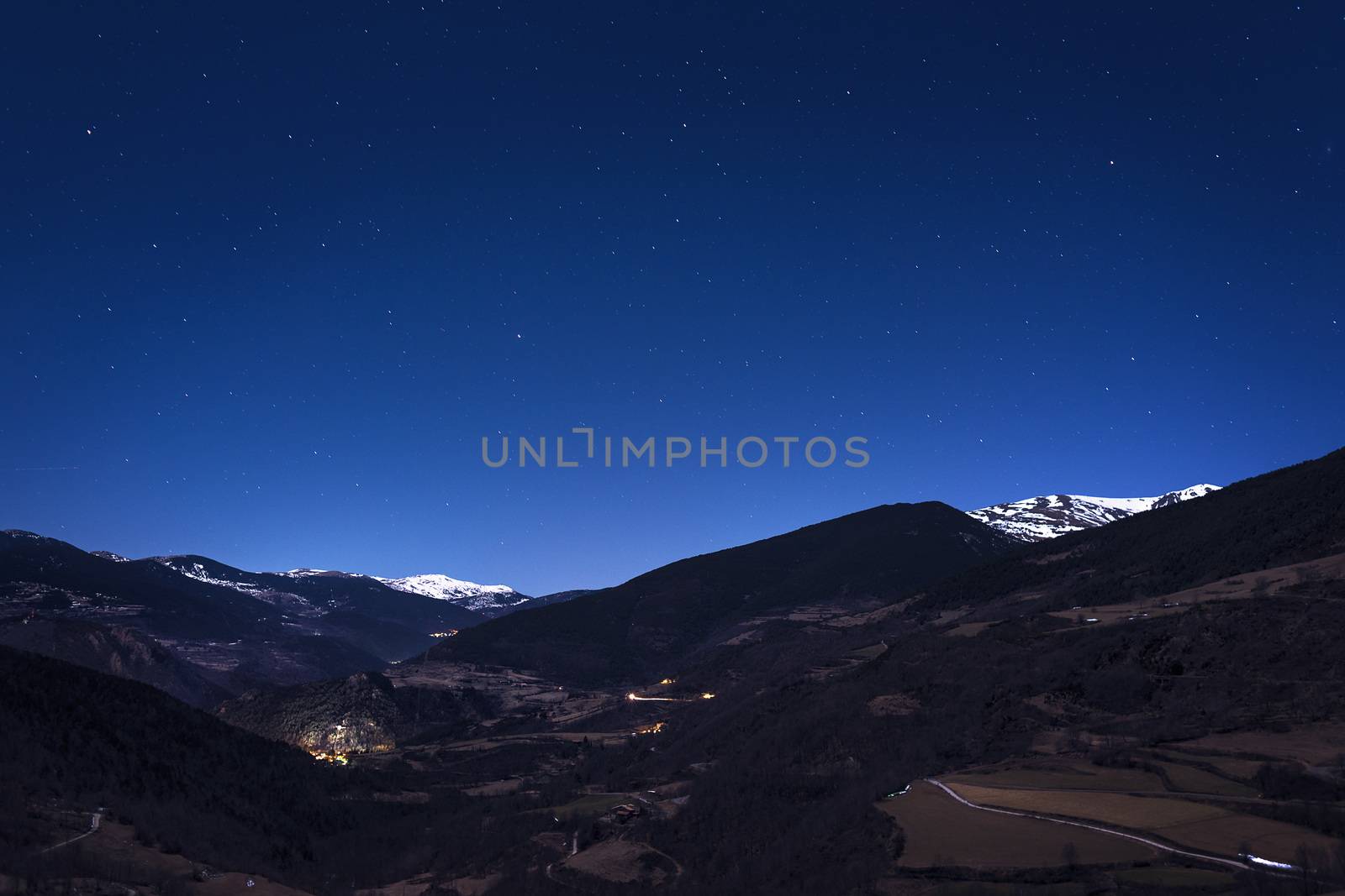 night mountain landscape under the starry sky, you can see the lights of the houses in the valley and some snowy mountains