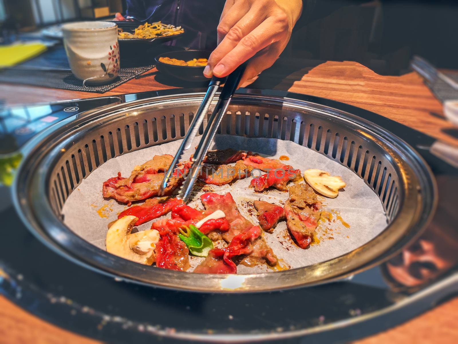 female hand cooking korean bulgogi griller beef in a bbq grill on restaurant table by LucaLorenzelli