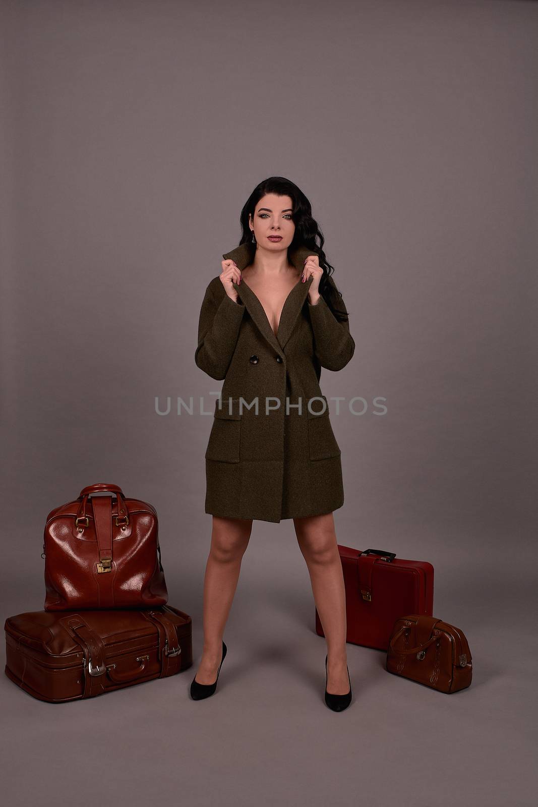 Studio portrait of a woman in classic coat posing on a gray background. Set of retro suitcases and hand bag. The concept of  tourism, recreation and travel advertising for designers with copy space.