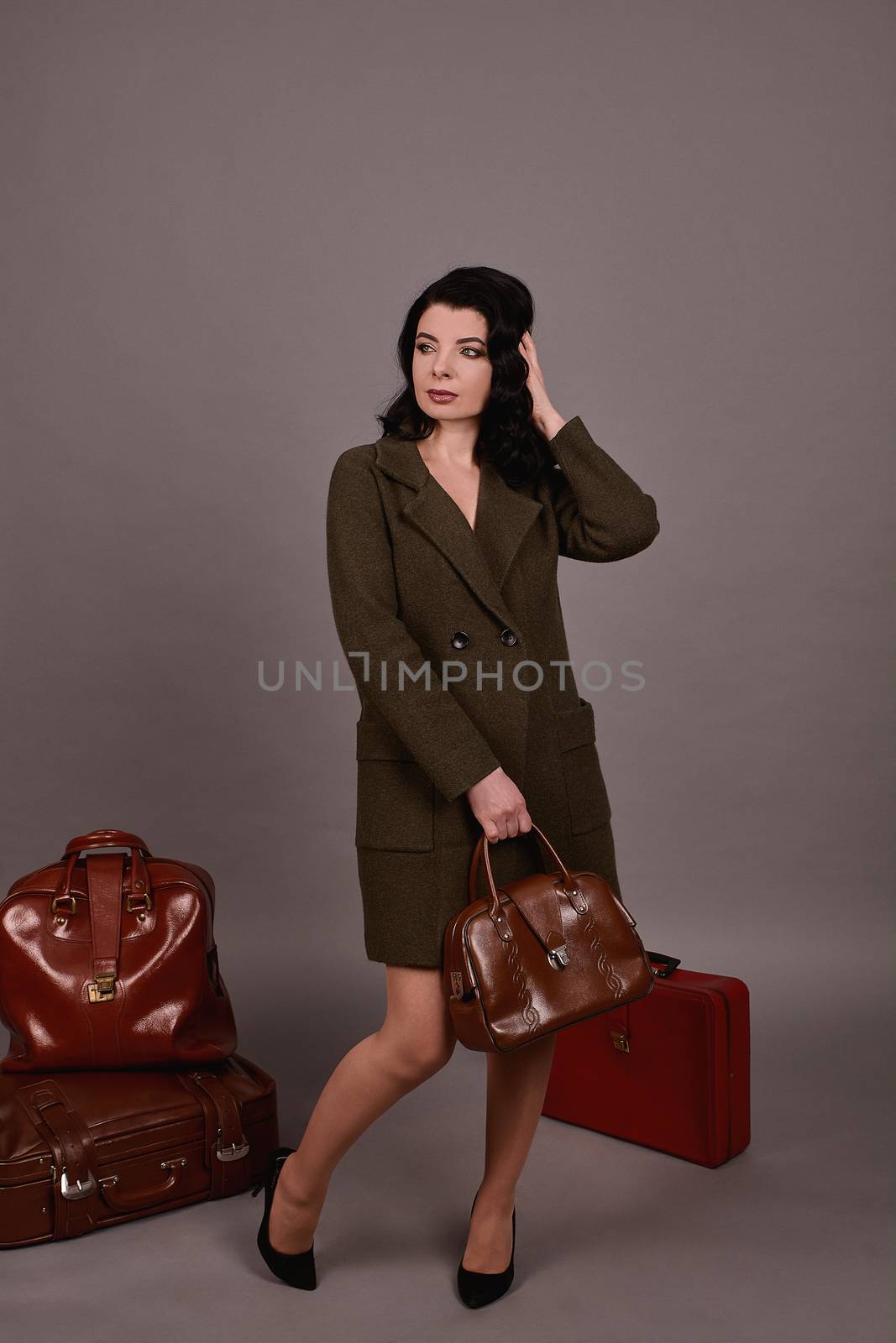 Studio portrait of a woman in classic coat posing on a gray background. Set of retro suitcases and hand bag. The concept of  tourism, recreation and travel advertising for designers with copy space.
