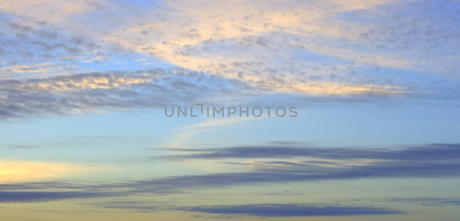 The blue sky at dawn, the sun's rays break through the clouds, painting them orange. The picture was taken in the autumn warm morning.