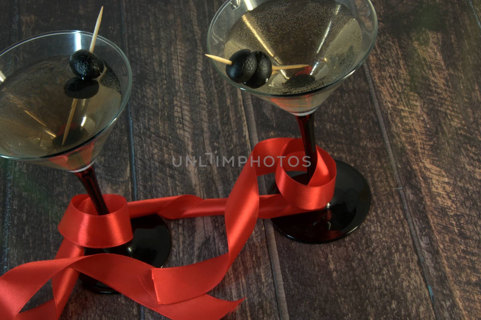 Two martini glasses with olives, with a scarlet ribbon on a wooden table Close-up.