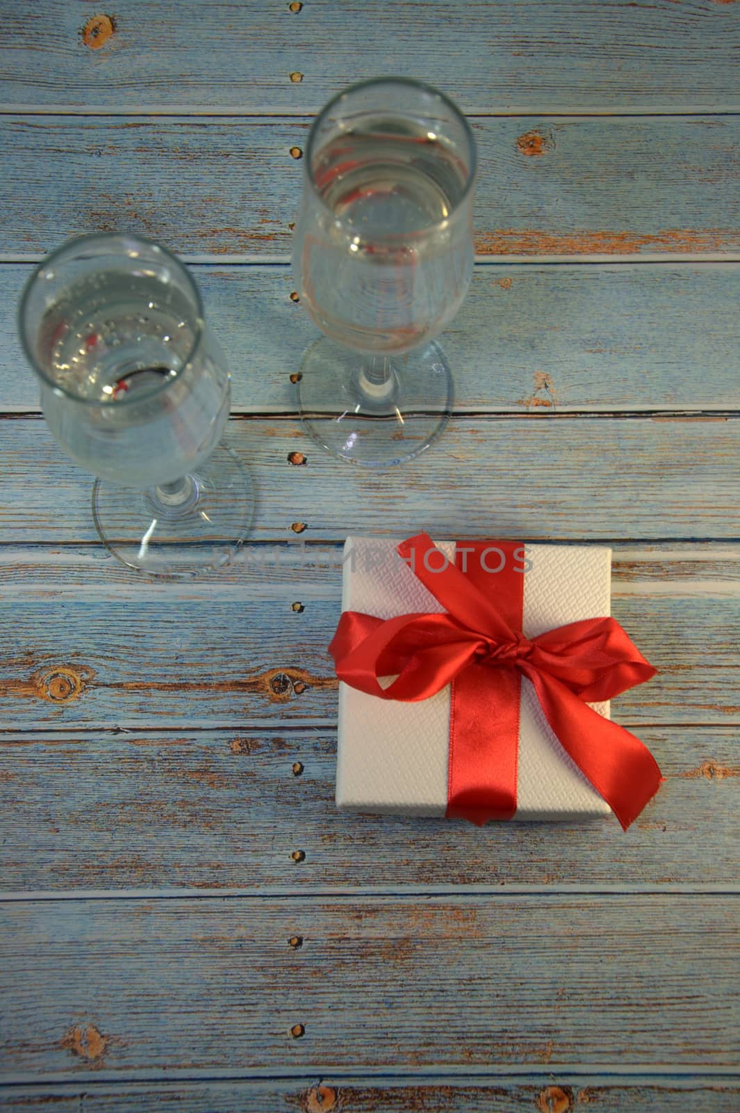 Two glasses with champagne and gift box with satin ribbon on a wooden table. by alexey_zheltukhin