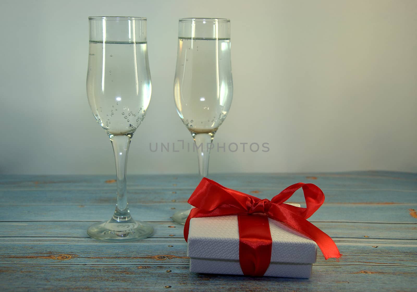 Two glasses with champagne and gift box with satin ribbon on a wooden table. Close-up.