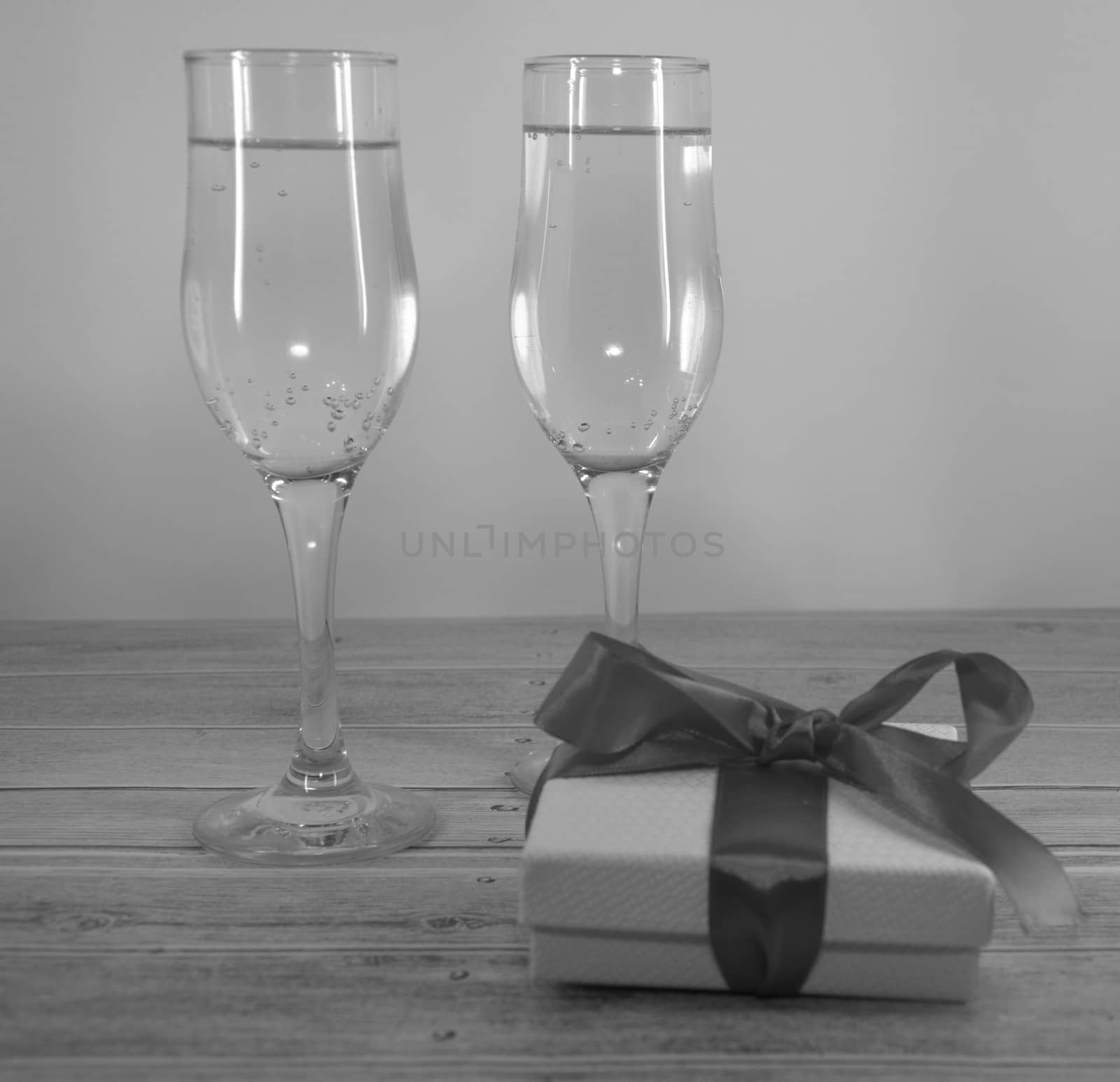 Two glasses with champagne and gift box with satin ribbon on a wooden table. Close-up.