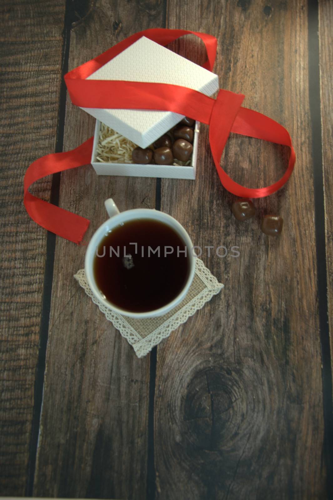 A cup of tea, a white box of chocolates with a red satin ribbon on a wooden table. Close-up.