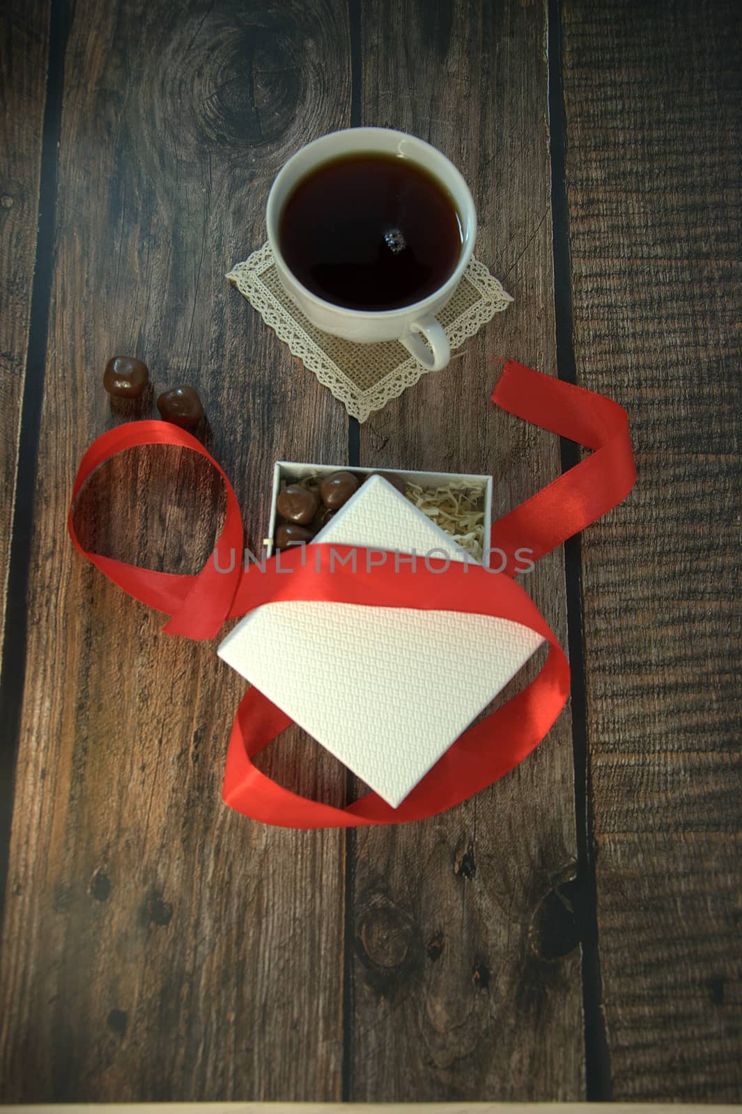 A cup of tea, a white box of chocolates with a red satin ribbon on a wooden table. Close-up.