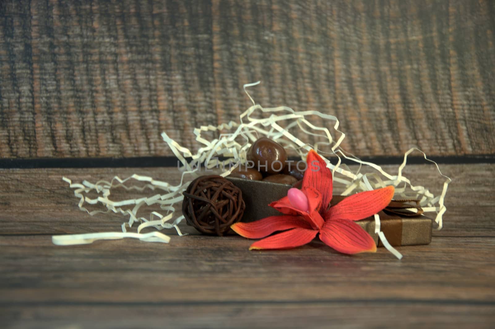 A box of chocolates, decorative balls, a bud of red orchid and hay on a wooden table.Close-up.