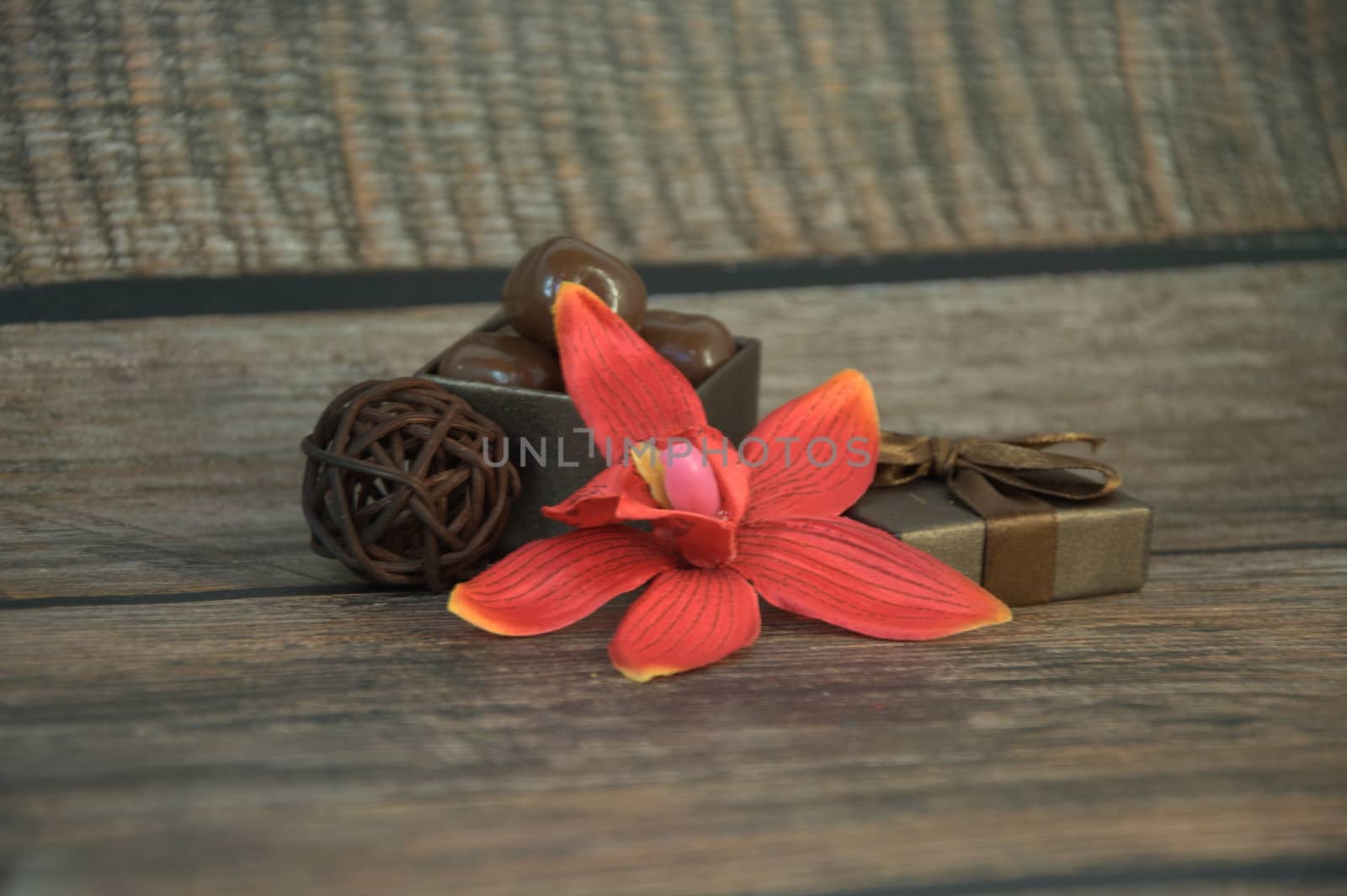A box of chocolates, decorative balls, a bud of red orchid on a wooden table. Close-up.