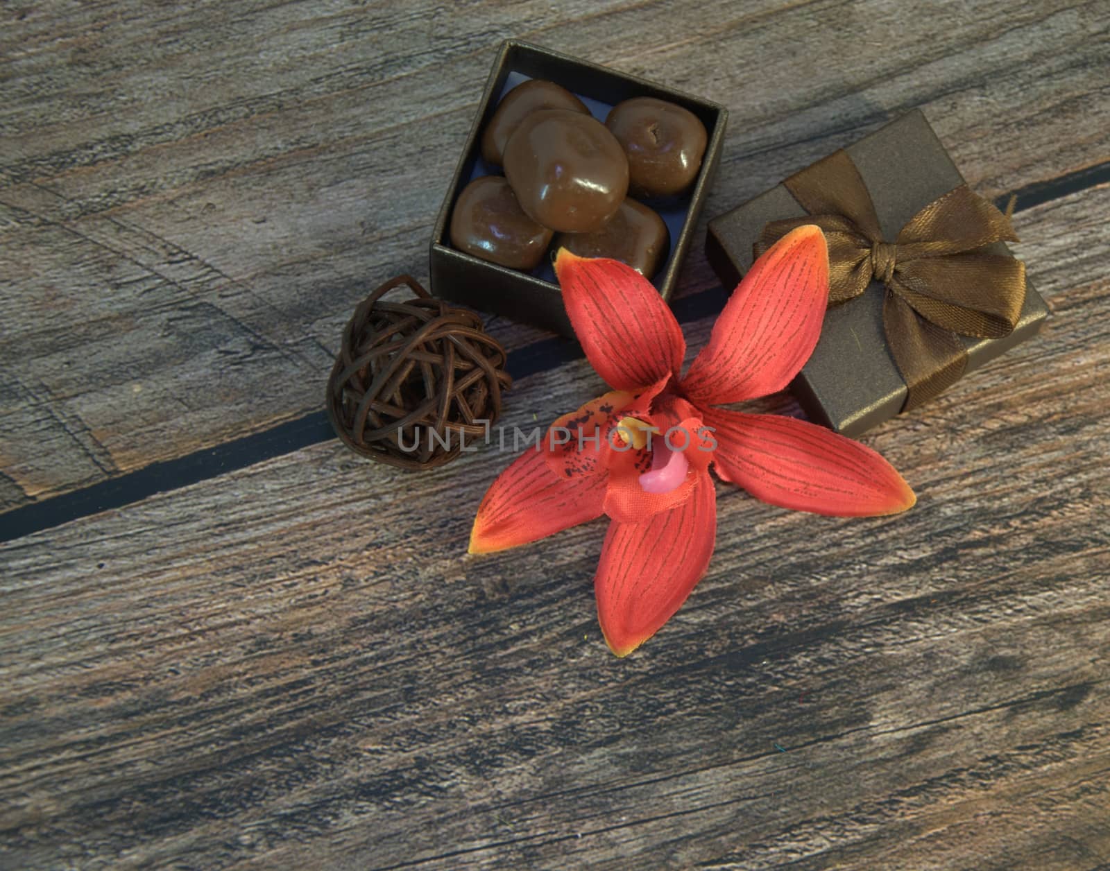 A box of chocolates, decorative balls, a bud of red orchid on a wooden table. Close-up.