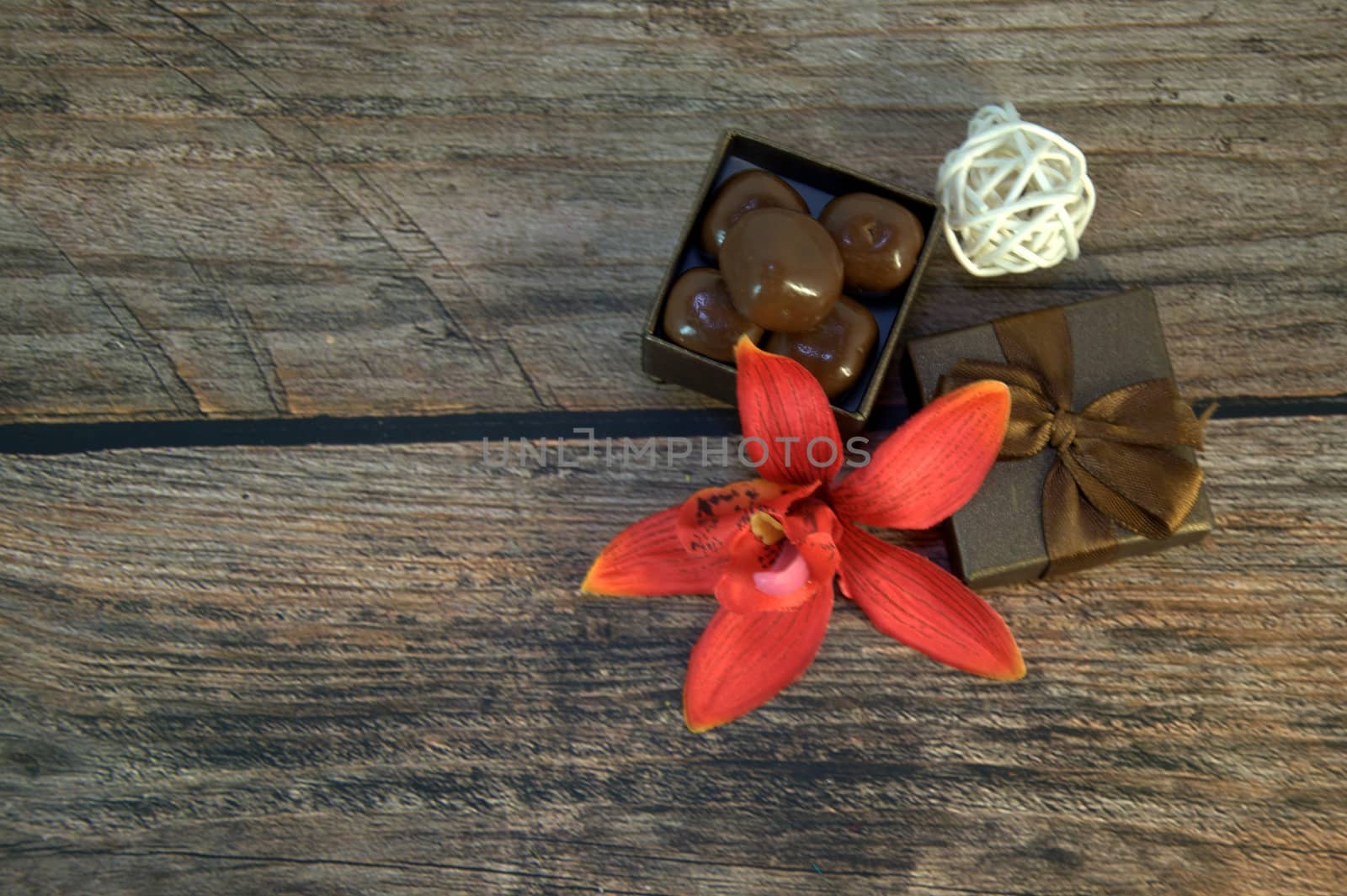A box of chocolates, decorative balls, a bud of red orchid on a wooden table. Close-up.