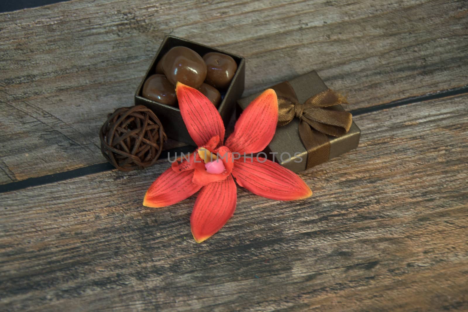 A box of chocolates, decorative balls, a bud of red orchid on a wooden table. Close-up.