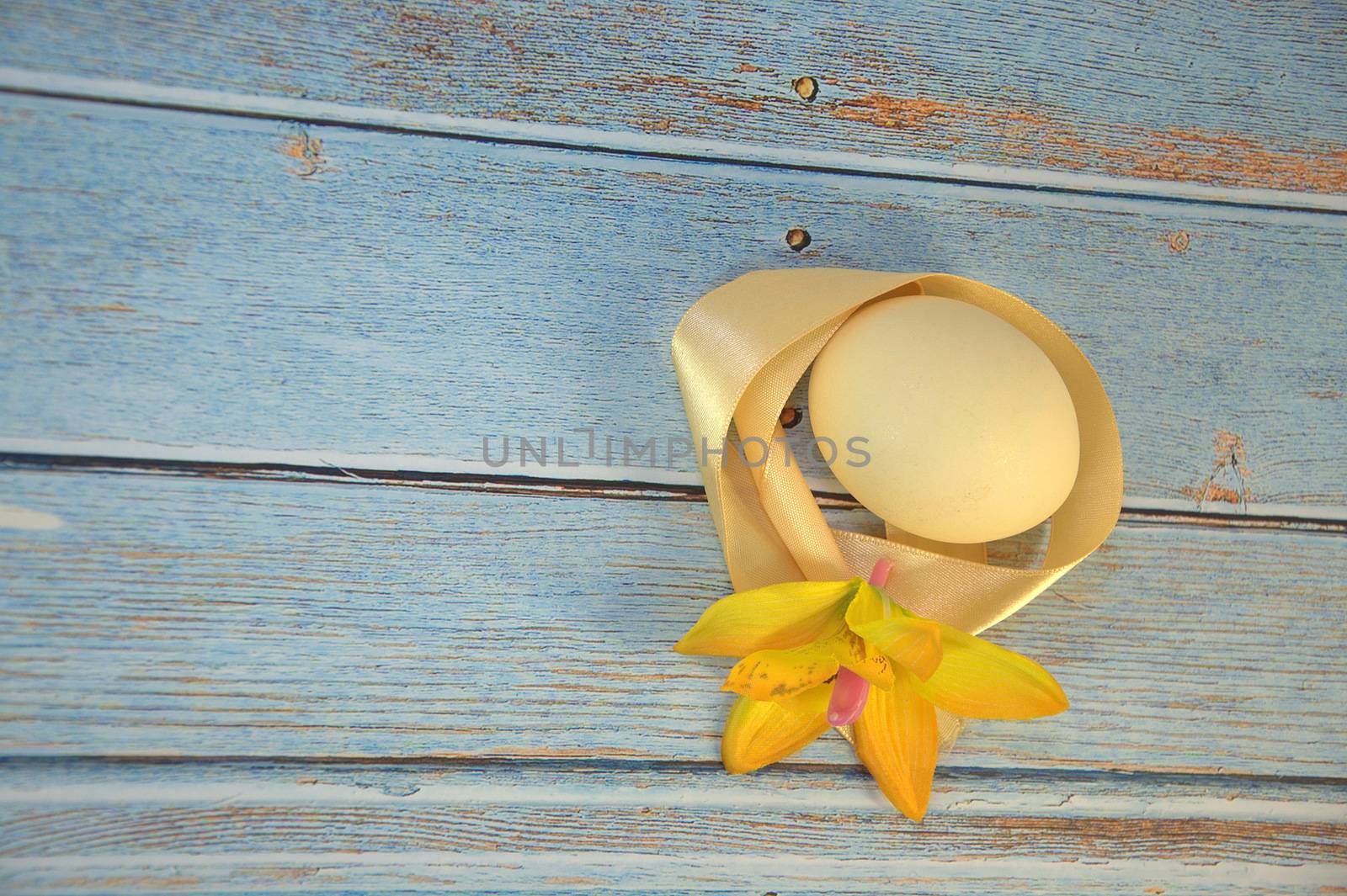 Easter egg with a yellow satin ribbon and a bud of an orchid on a wooden table. Close-up.