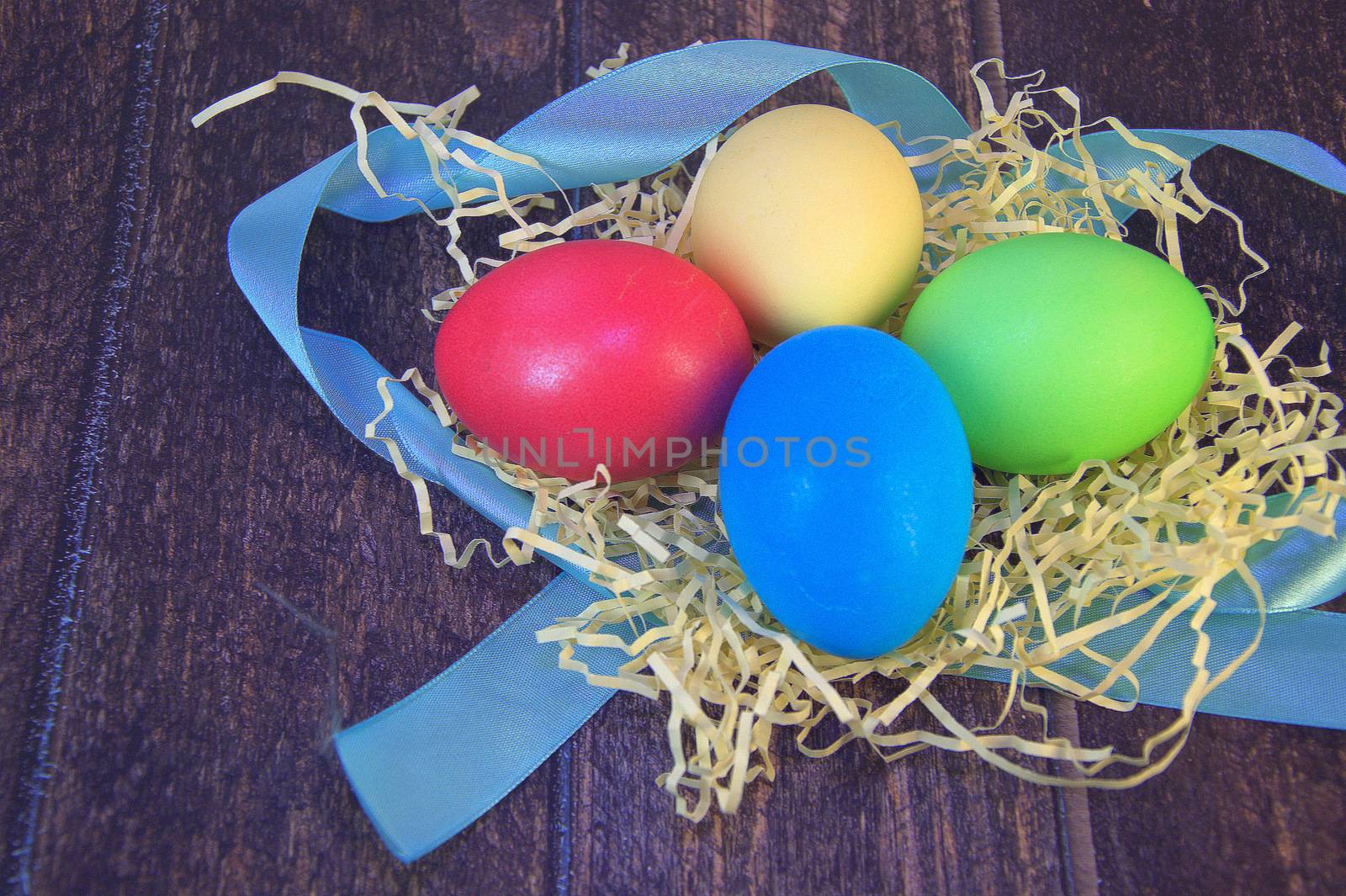 Painted Easter eggs in a nest of straw on a blue ribbon lie on a wooden table. by alexey_zheltukhin