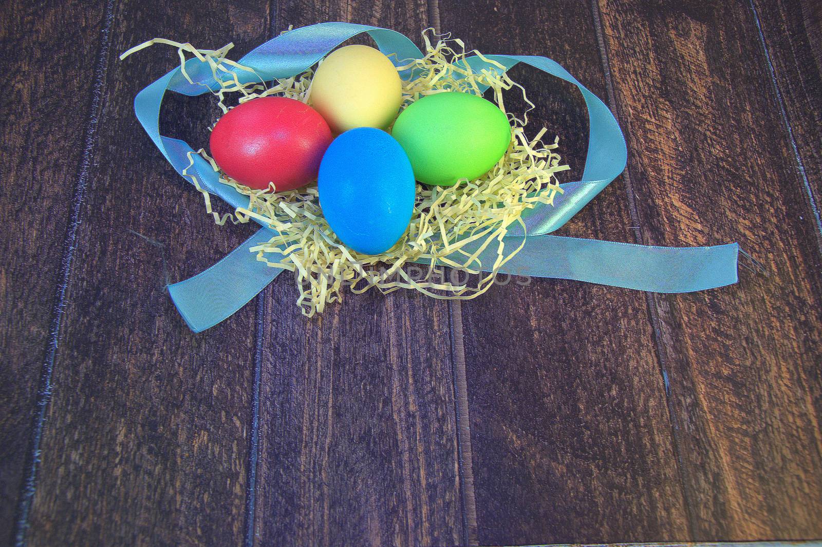 Painted Easter eggs in a nest of straw on a blue ribbon lie on a wooden table. by alexey_zheltukhin