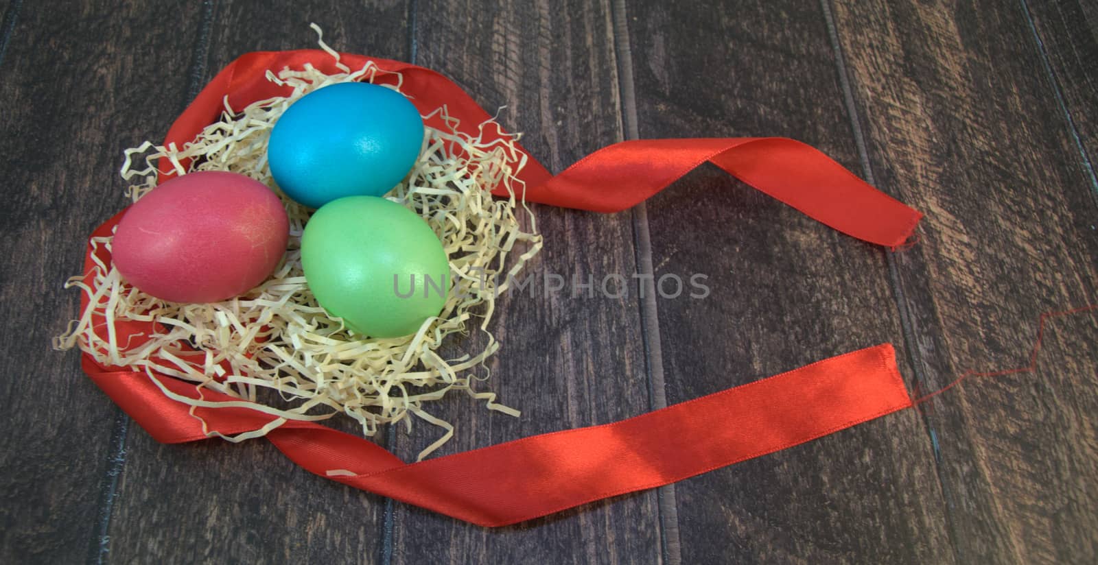 Painted Easter eggs in a nest of straw on a scarlet ribbon lie on a wooden table. Close-up.