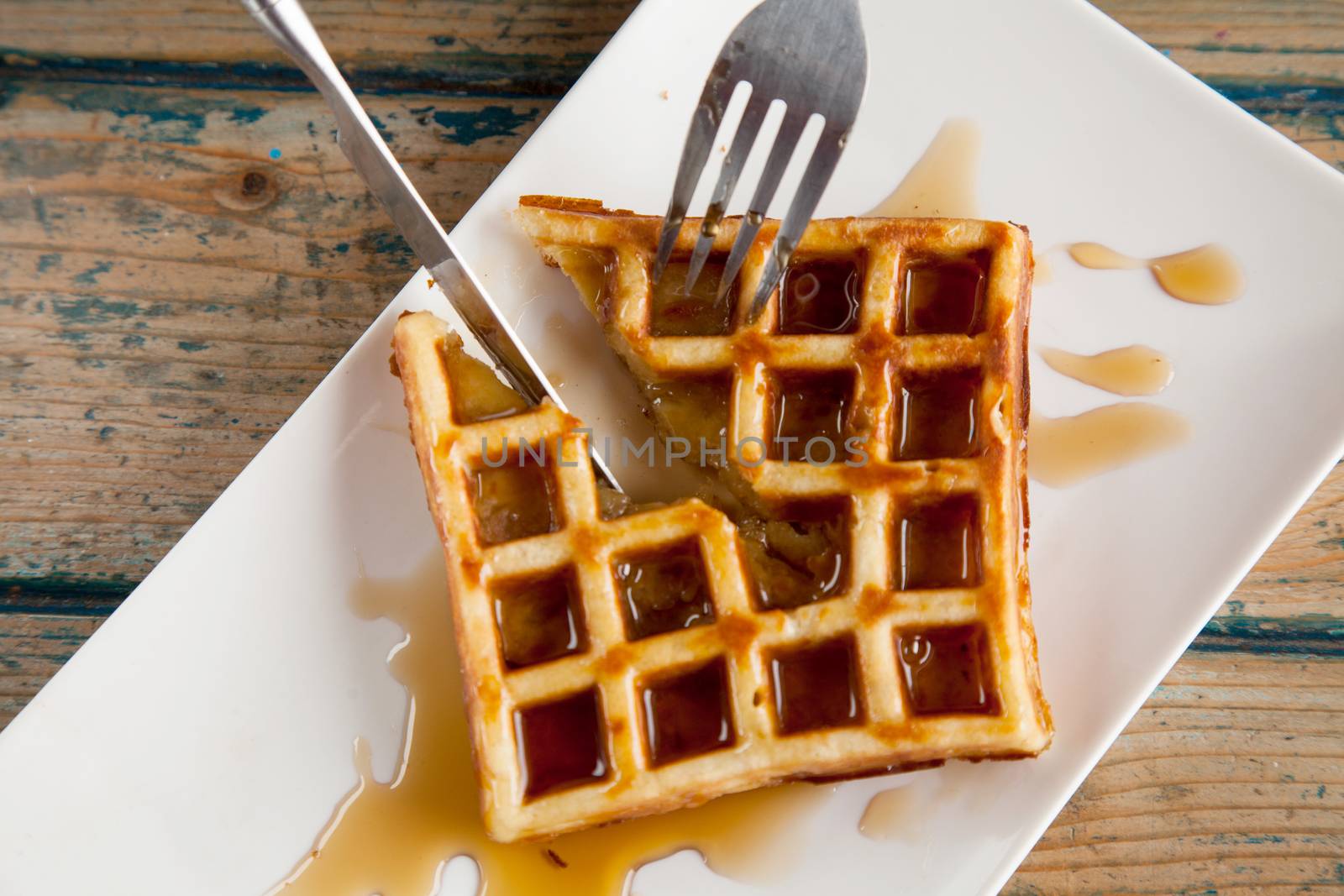 Waffle with maple syrup cutting in half with knife and a fork