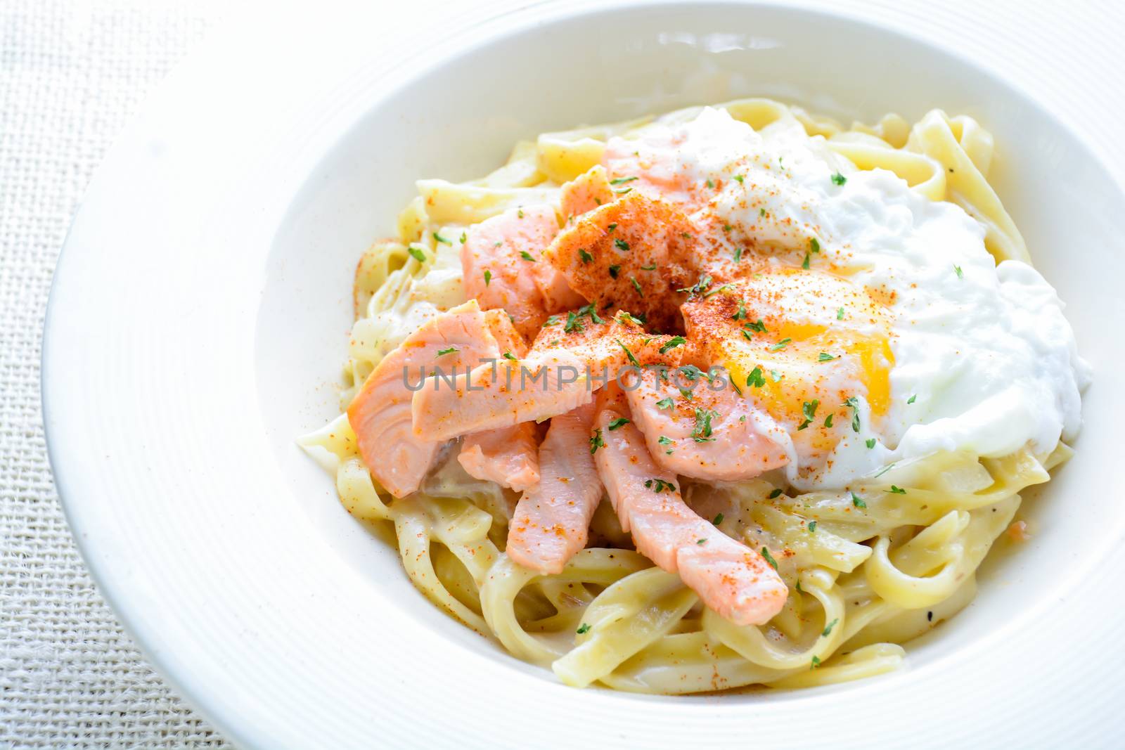 Fettucine with salmon, egg and parmesan cheese, served on white plate.